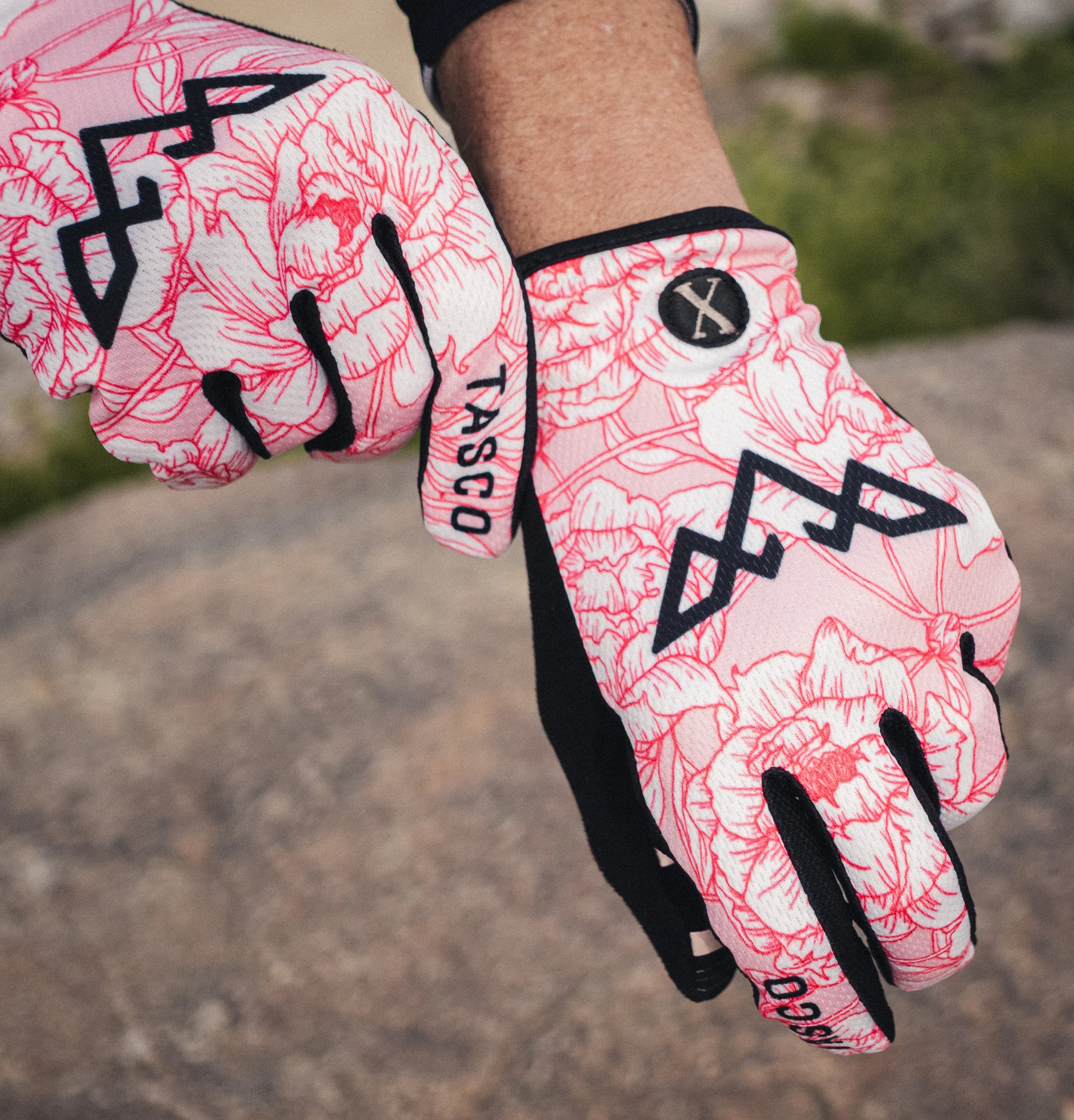 Close-up of a person's arm and hand wearing pink golf gloves with black accents and floral pattern, with grass background.