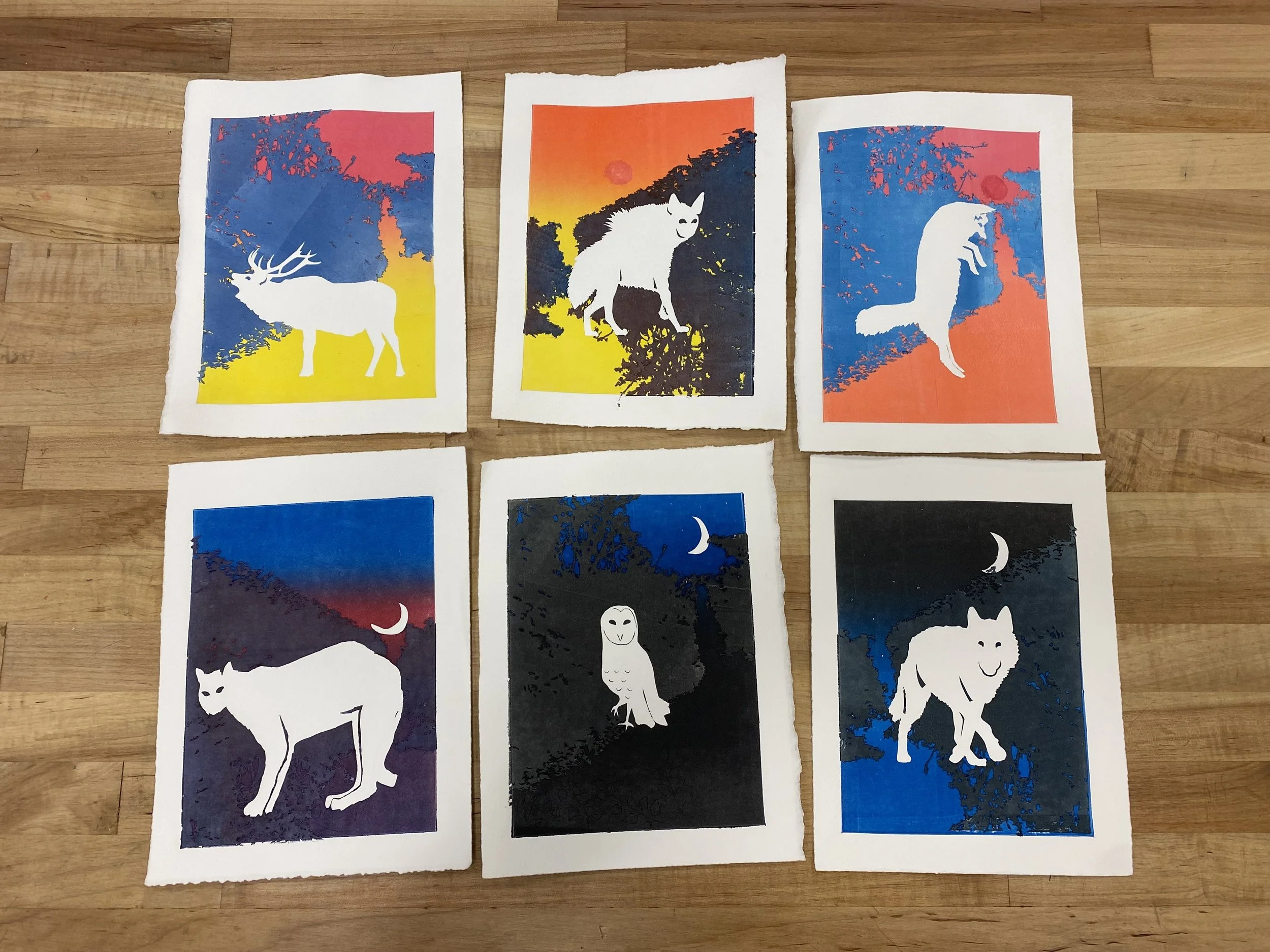 Six colorful prints with white animals sit on a wooden table