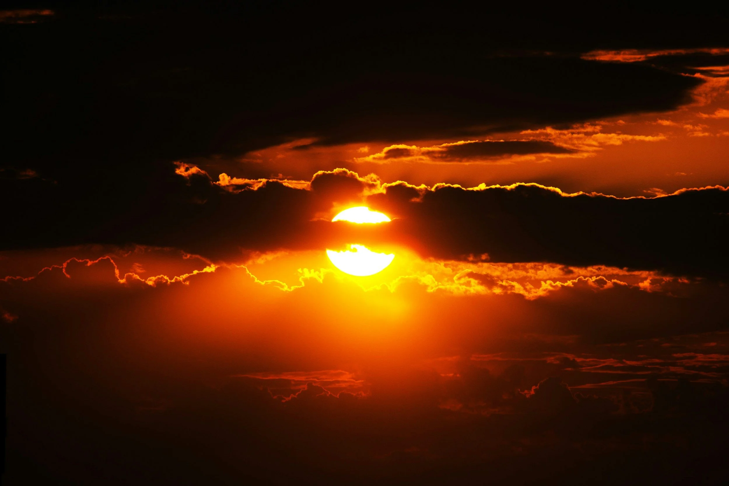 Sunset with the sun partially behind clouds, creating a bright glow and orange hues in the sky.