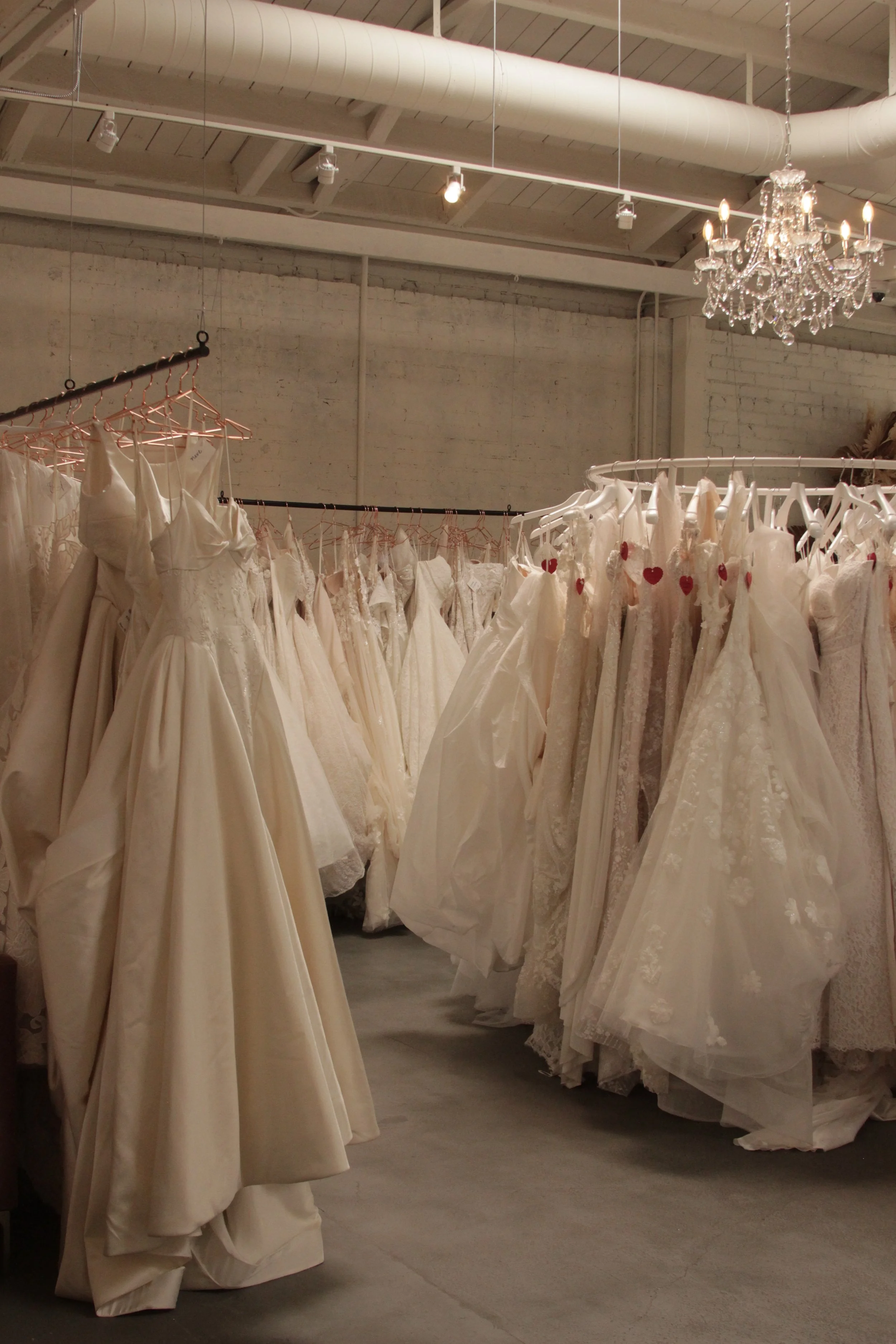 Bridal gowns on racks in a boutique or bridal shop with a chandelier hanging from the ceiling.
