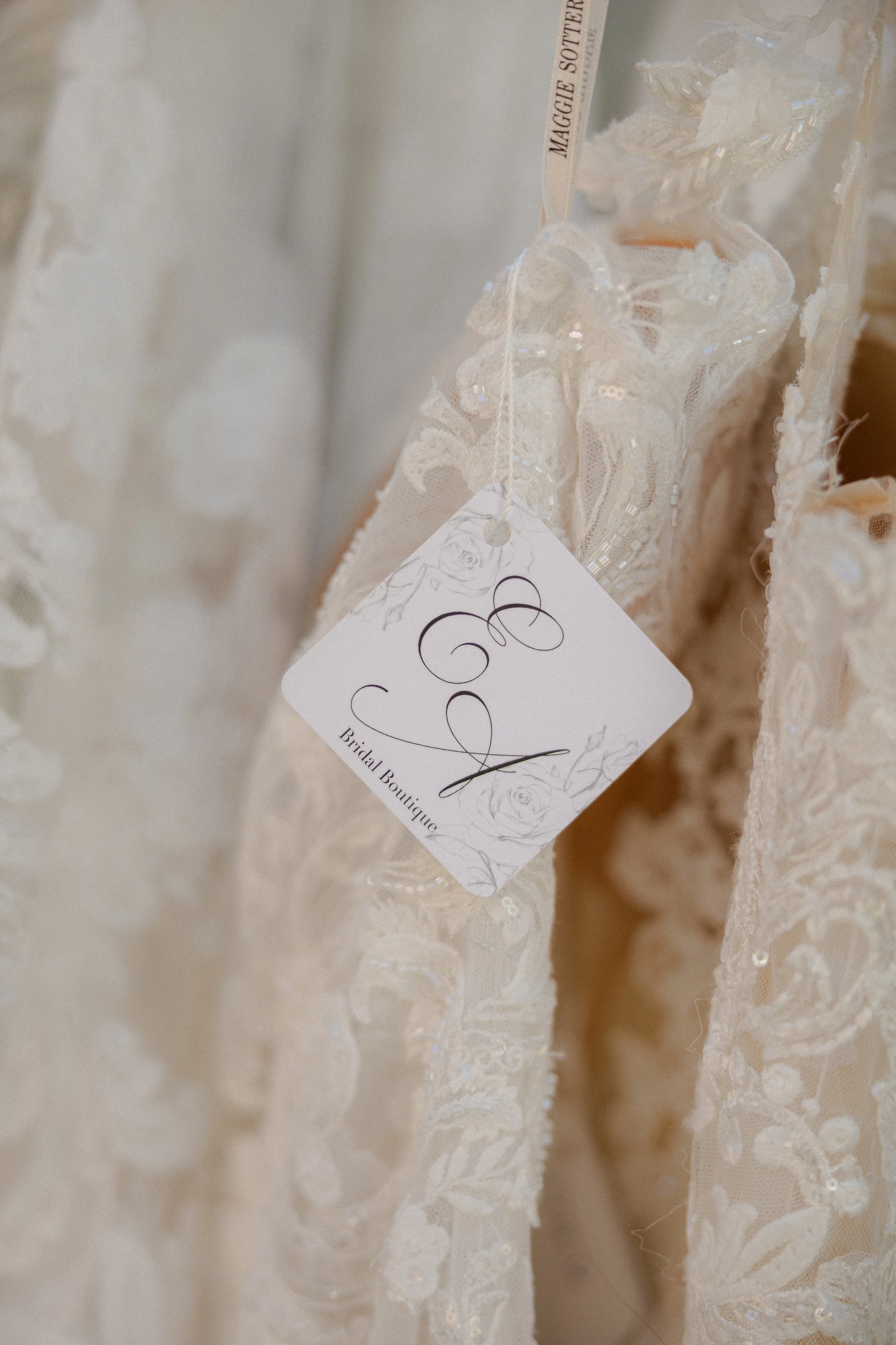 Close-up of a wedding dress with lace and bead details, featuring a bridal boutique tag attached.