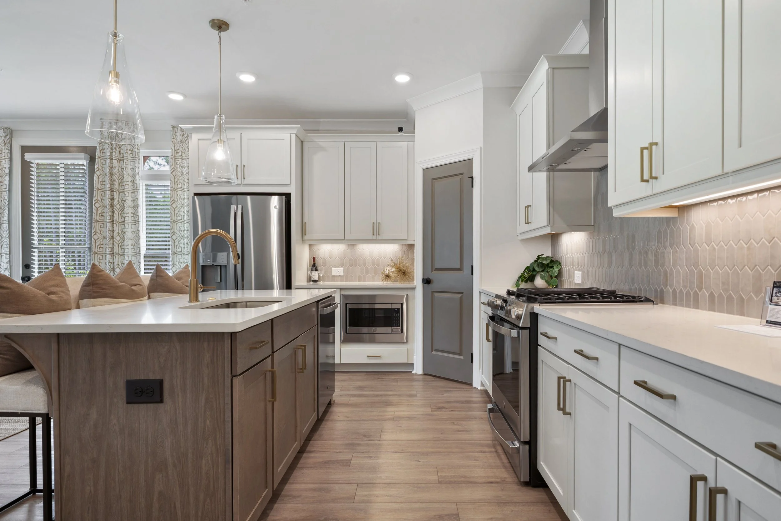 Modern kitchen with white cabinetry, stainless steel appliances, a kitchen island with a wooden base, pendant lighting, and windows with patterned curtains.