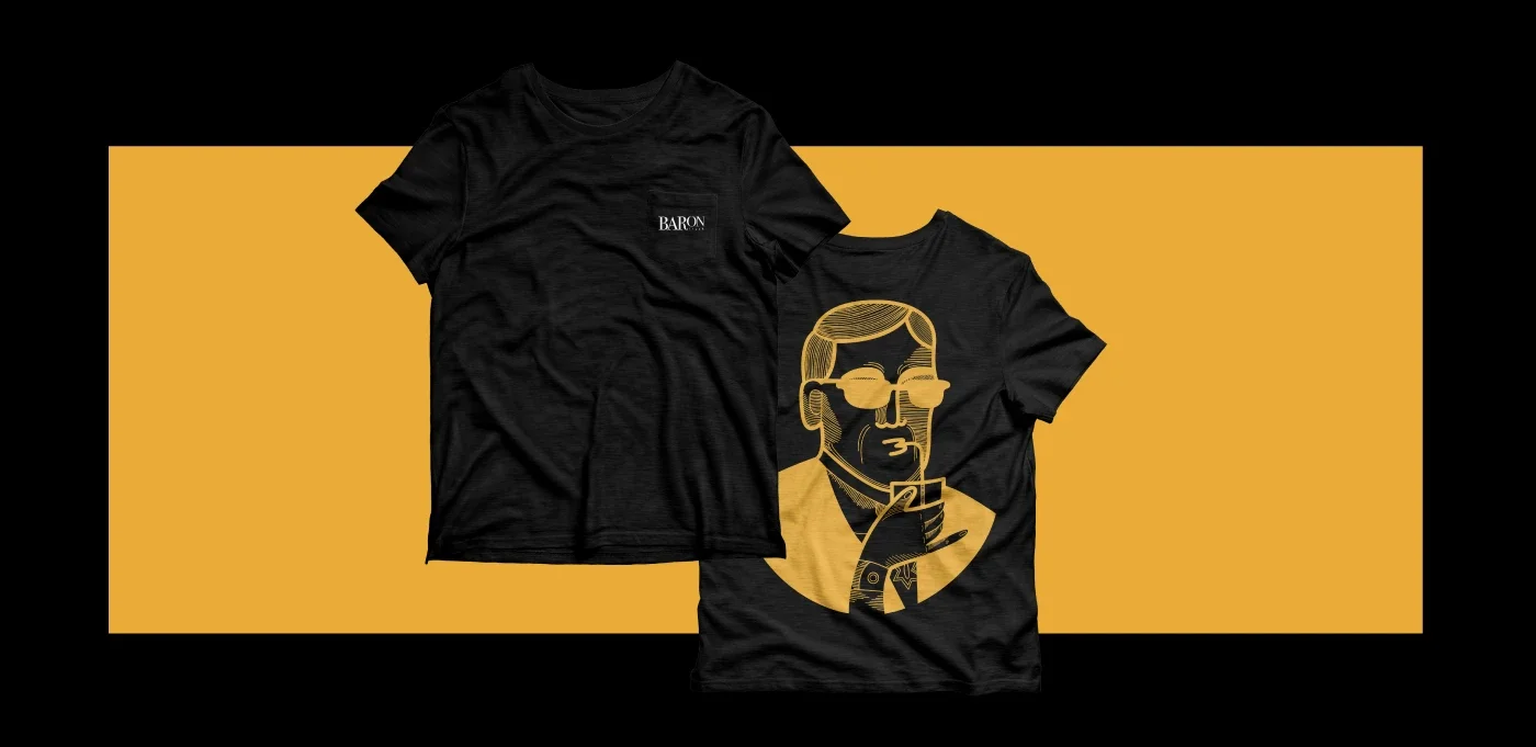 Duas camisetas pretas, uma com o logo 'BARON' e outra com um desenho de um homem usando óculos e segurando um celular.