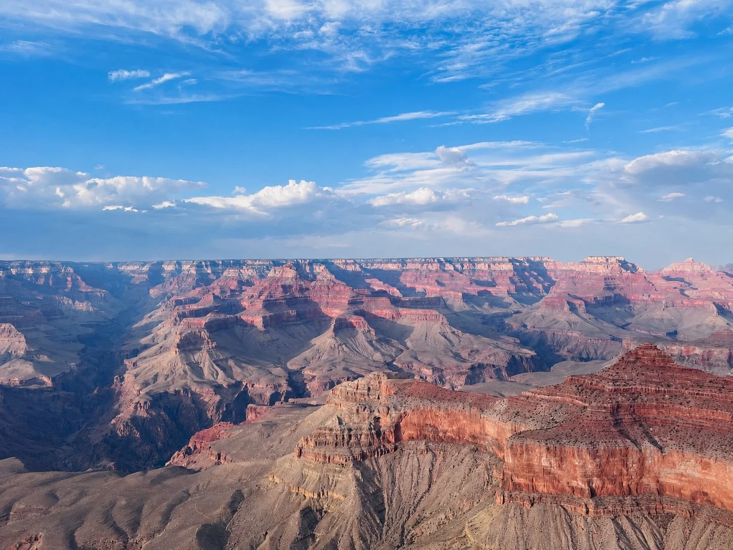 View of the Grand Canyon with layered red and brown rocks under a blue sky with scattered clouds