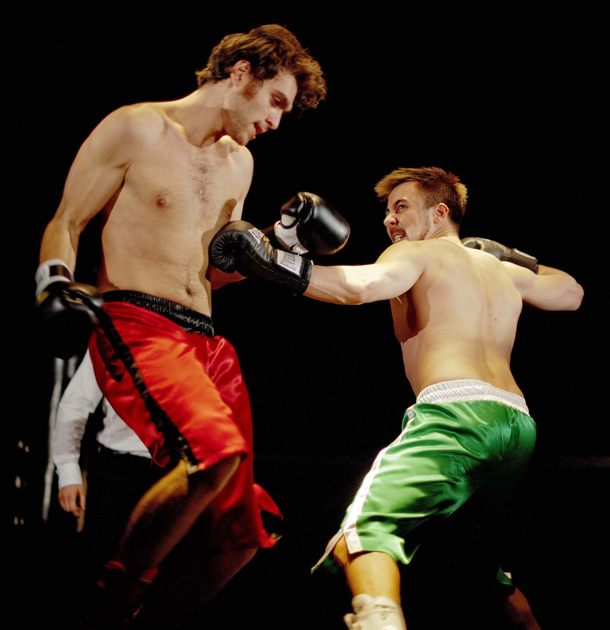 Two shirtless male fighters engaged in a boxing match, with one fighter throwing a punch at the other's face, against a black background.