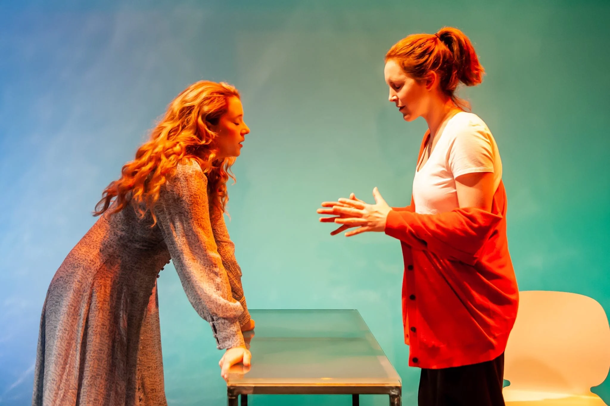 Two women with red hair are standing across from each other, holding hands, with a colorful background.