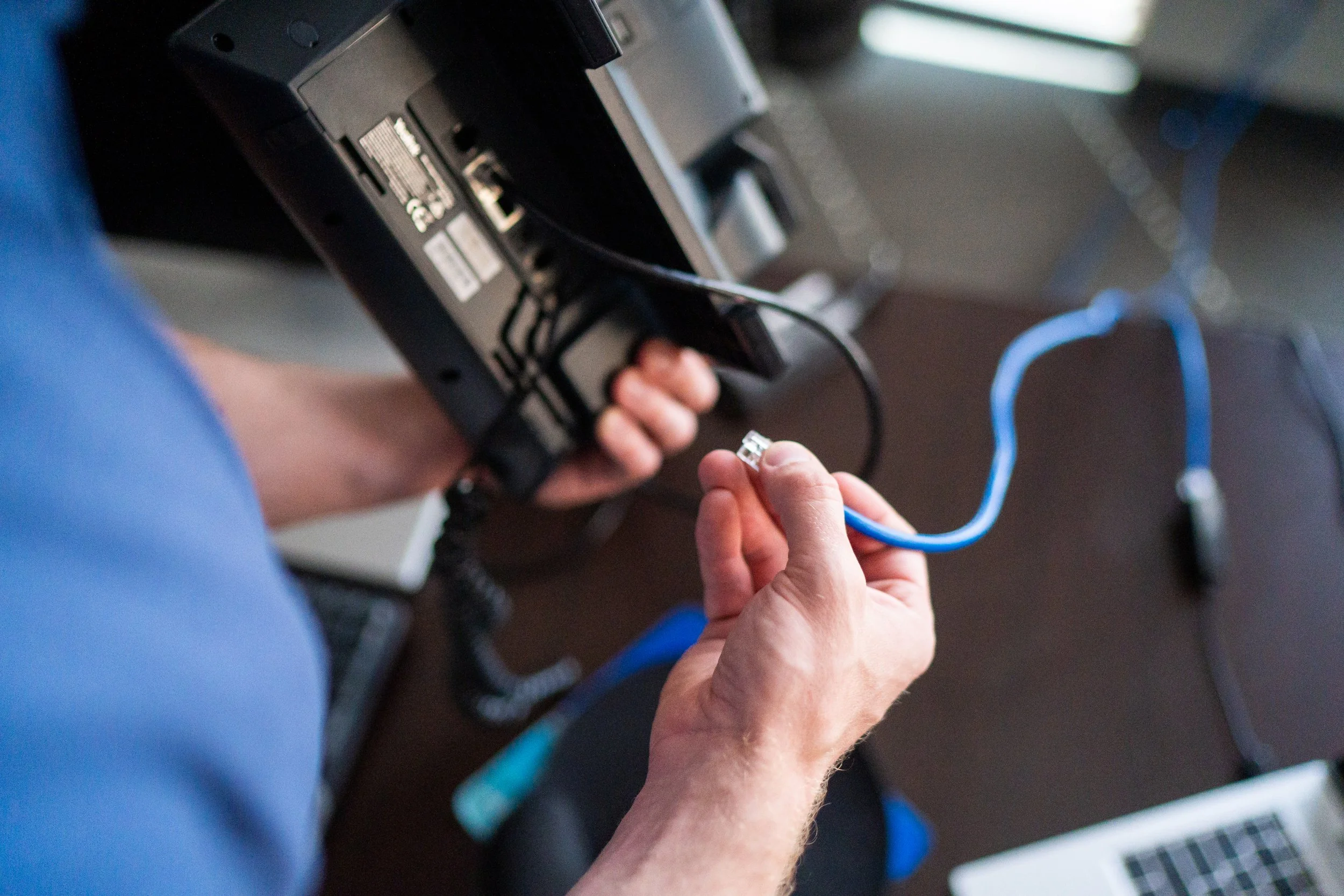 Person connecting a blue Ethernet cable into a black electronic device, such as a modem or router.