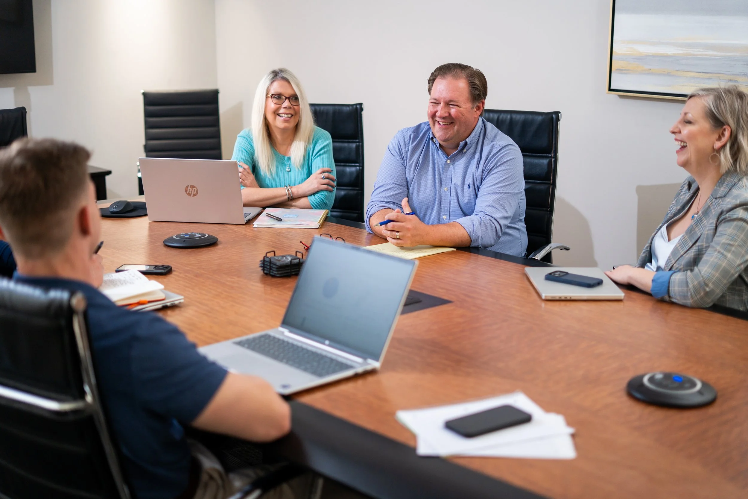 A group of people in a business meeting sitting around a conference table, smiling and talking.