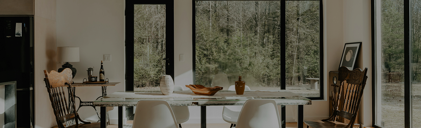 Dining room with large window overlooking outdoors, marble table with decorative items, and mixed wooden and white dining chairs.