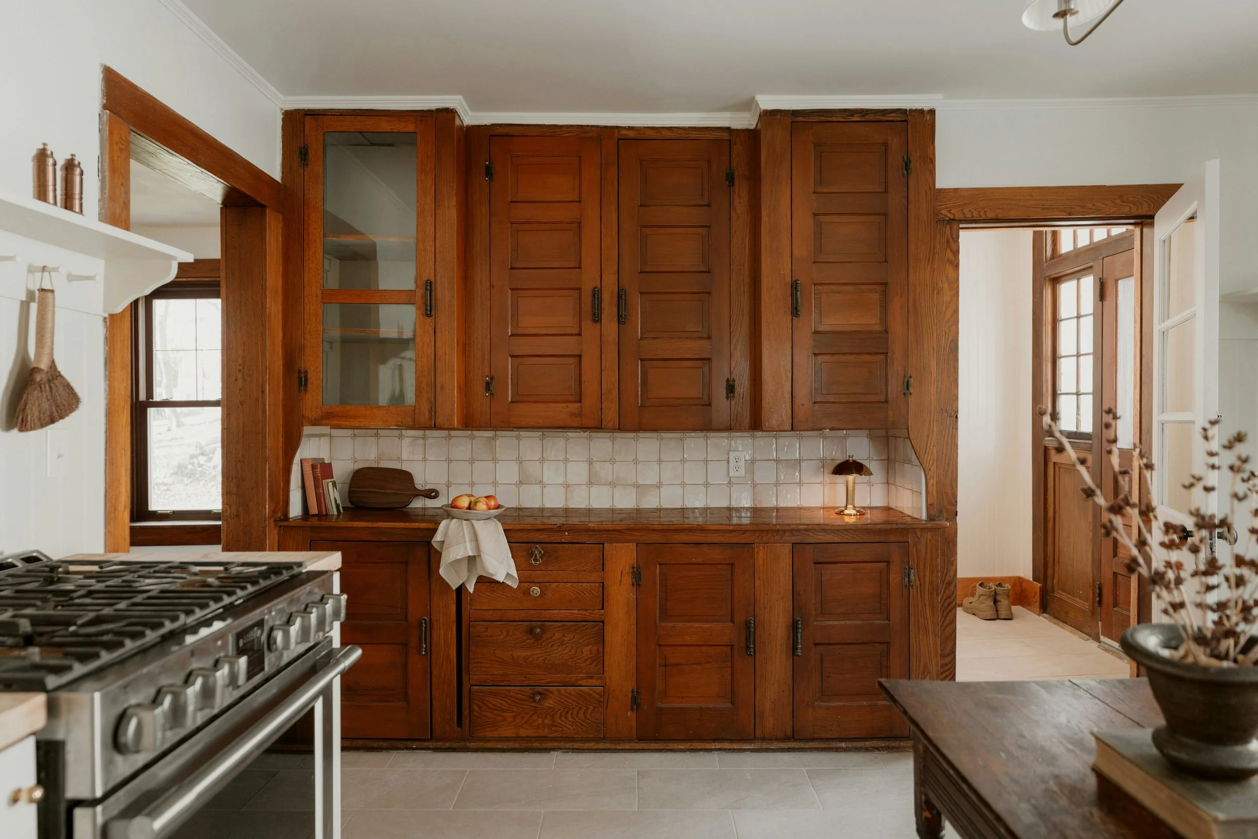 View of a kitchen with wooden cabinets, a stove in the foreground, and a window with a snow-covered landscape outside.
