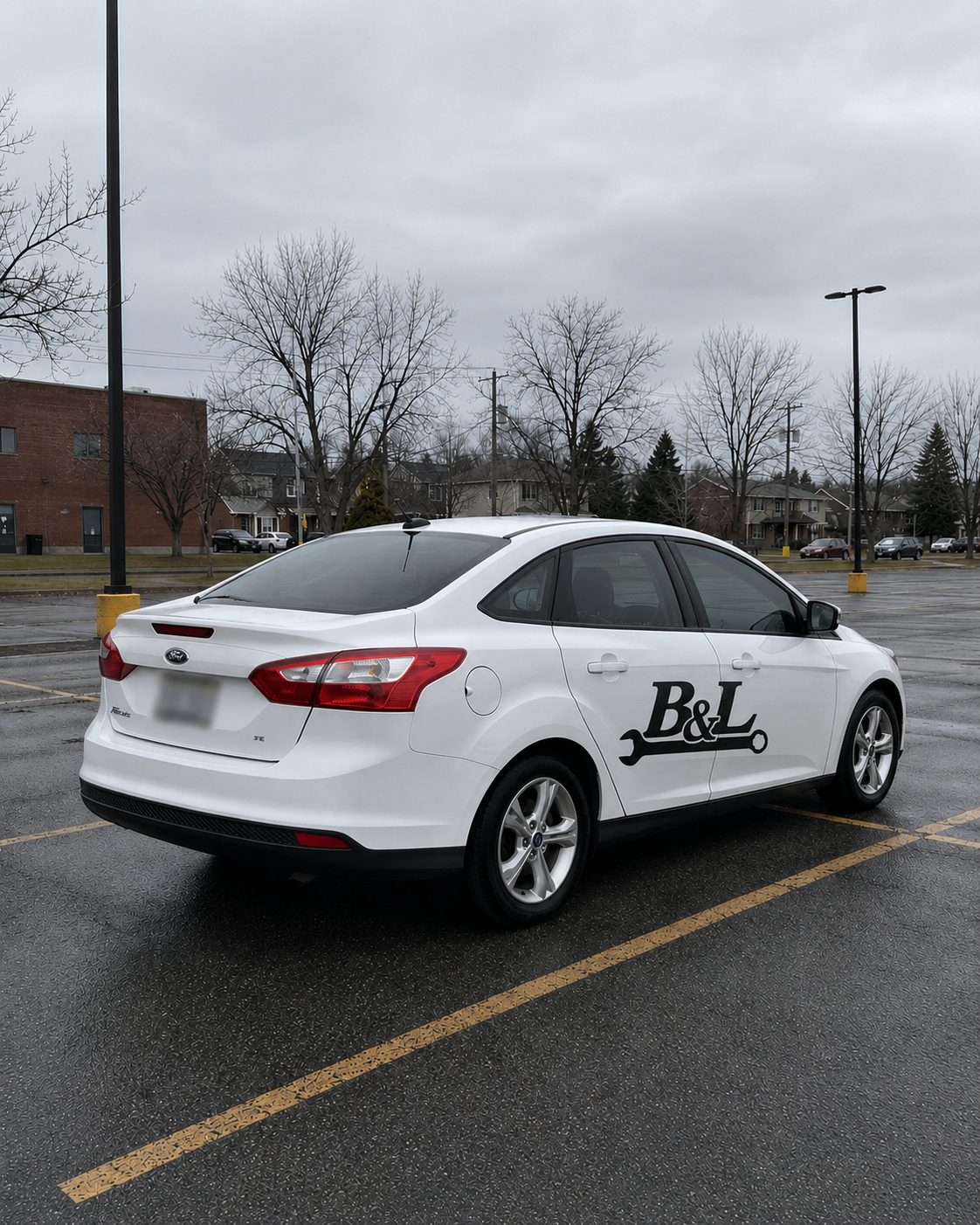 White sedan parked in an empty parking lot on a cloudy day, with a B&L logo featuring a wrench on the side.