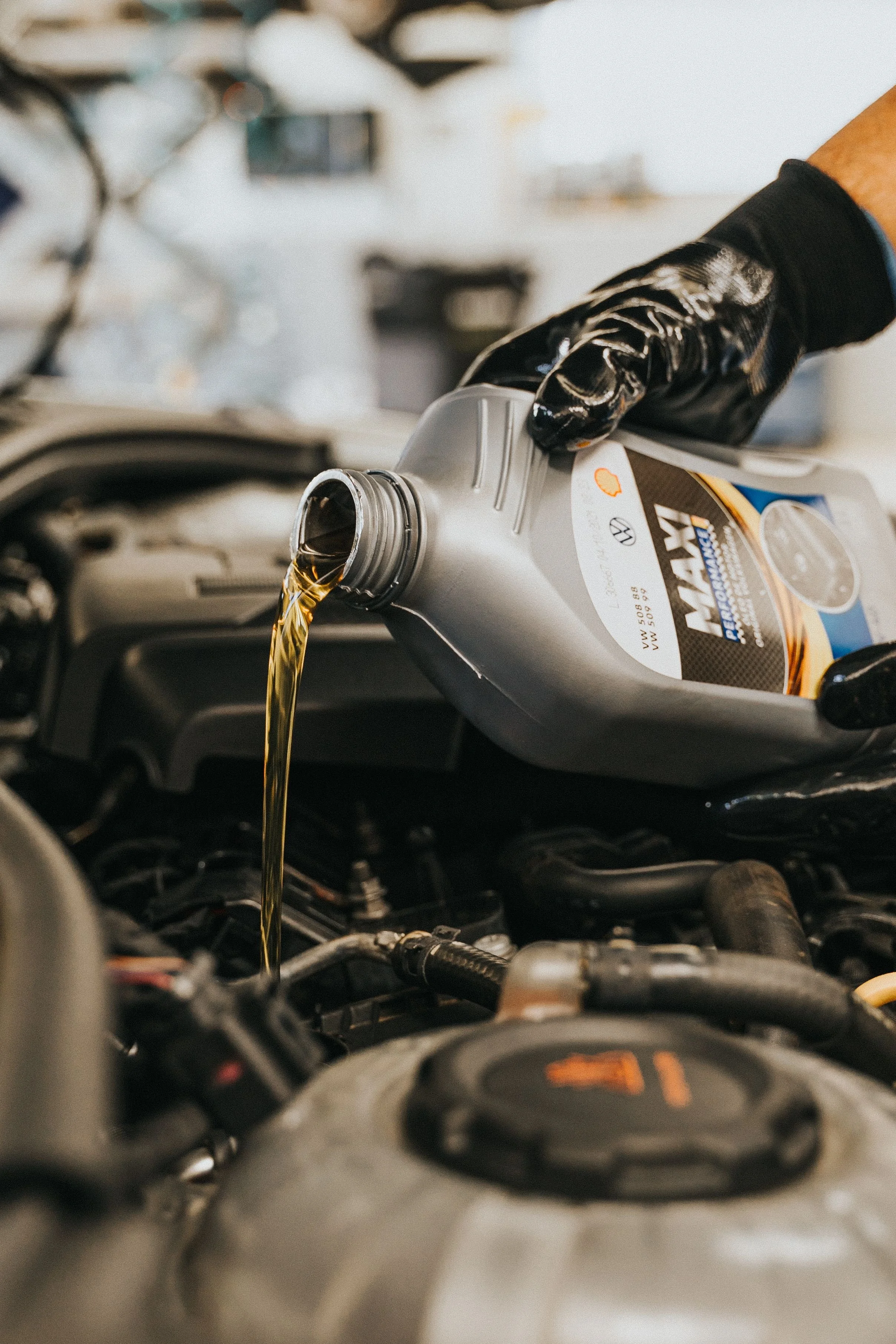 Motor oil is being poured from a bottle into a car engine. The person pouring the oil is wearing a black glove.