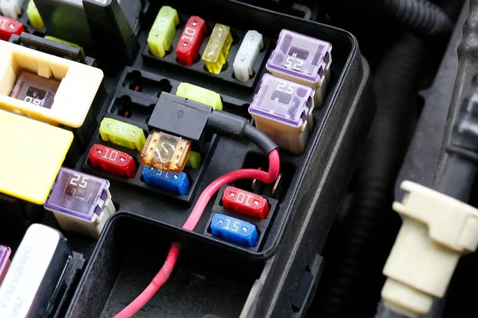 Close-up of a car's fuse box with various colored fuses and a red wire connected to a 10-amp fuse.