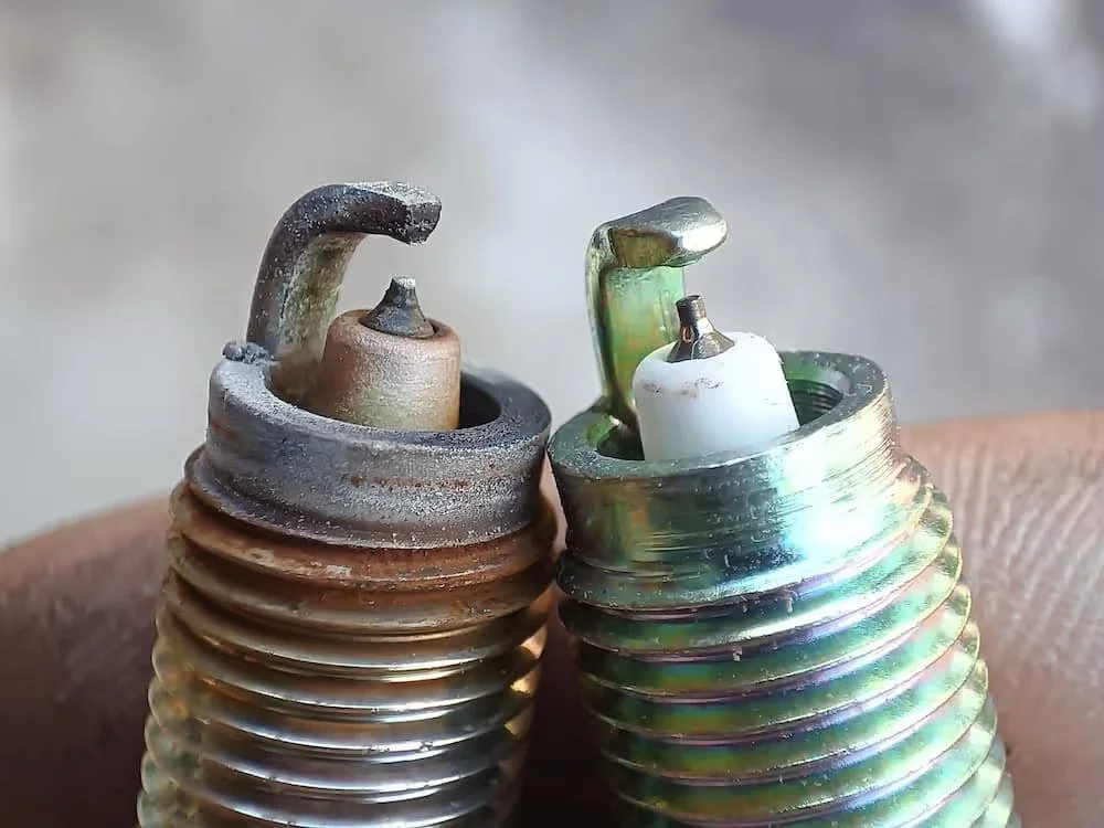 Close-up of two spark plugs, one old and rusty, the other new and shiny, placed on a person's skin.