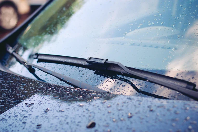 Close-up of a car windshield with raindrops, windshield wiper in focus, during rainy weather