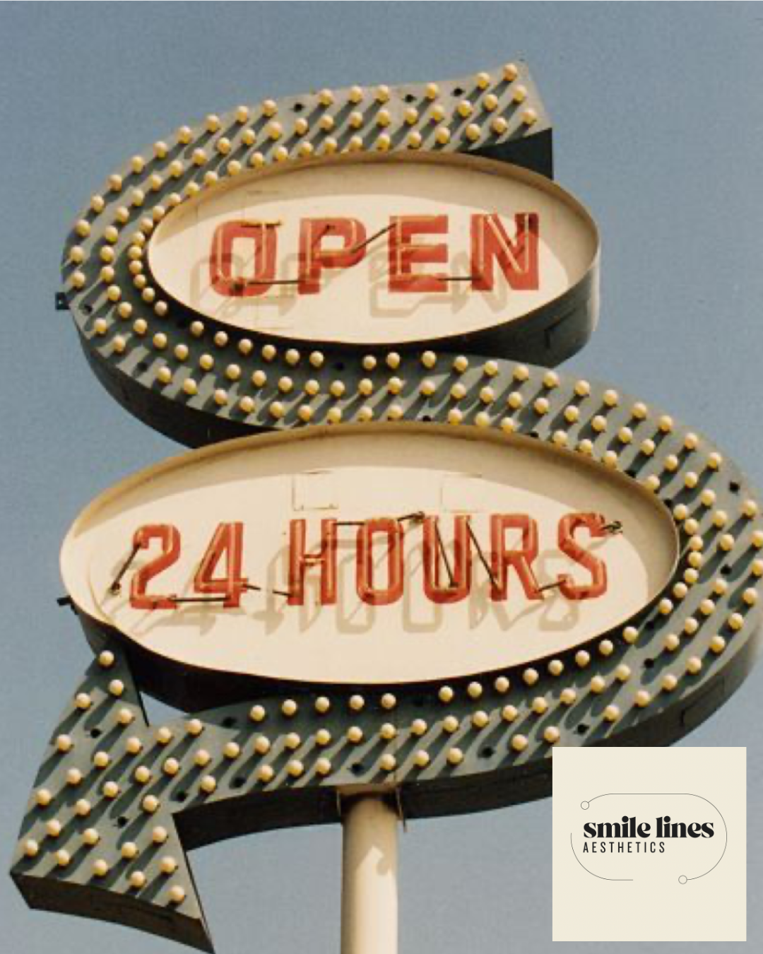 A vintage neon sign displays "OPEN 24 HOURS" with red letters, surrounded by a black border decorated with yellow bulbs, against a clear sky.