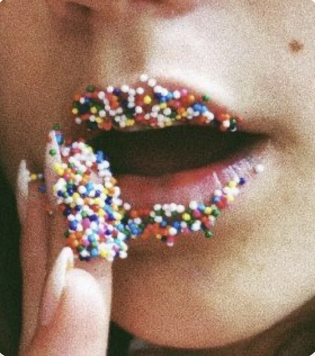 Close-up of parted lips covered with colorful round sprinkles, with a finger touching the lower lip.