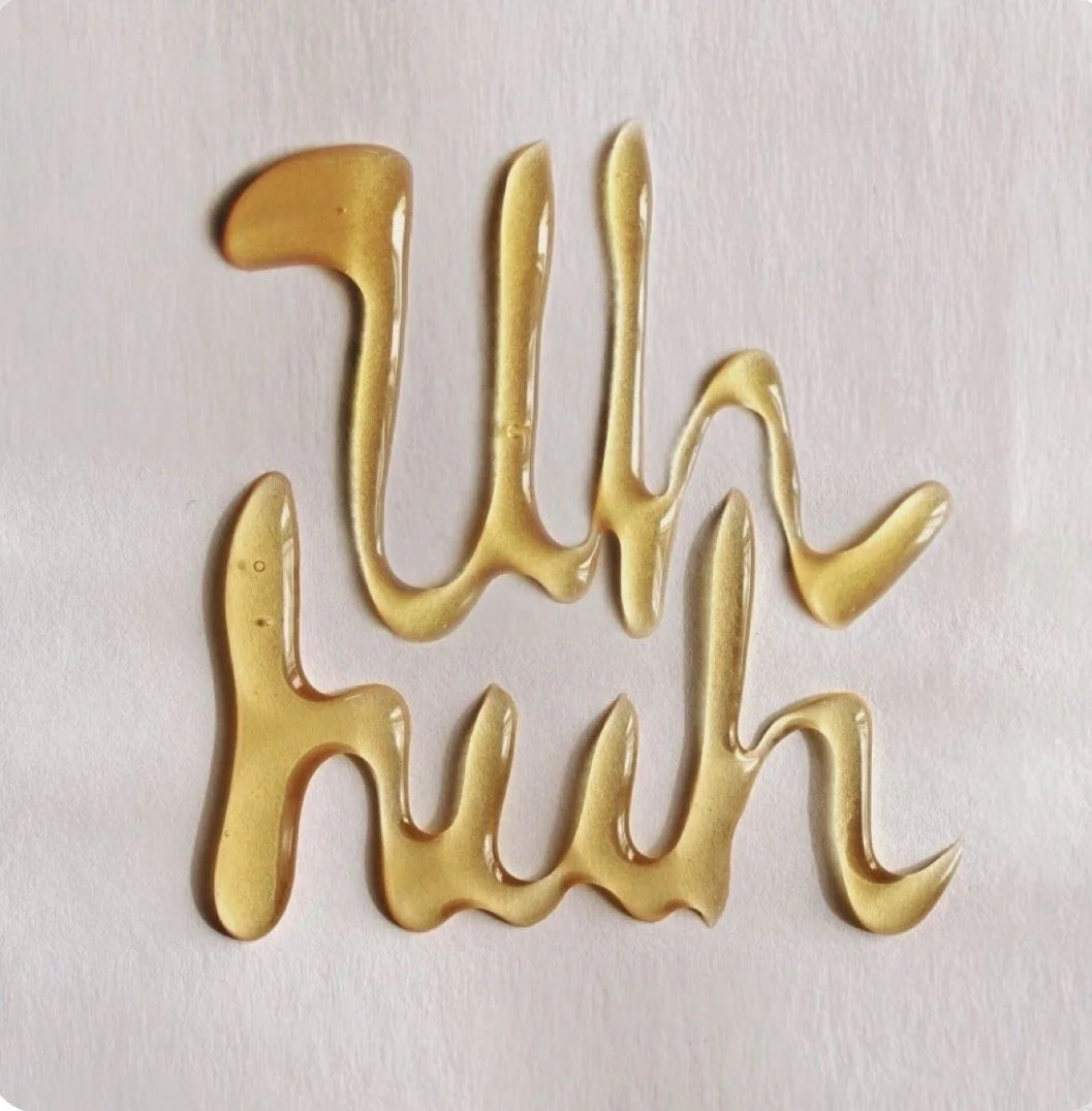The phrase "Cyber Mom" written in gold-colored syrup on a white surface.