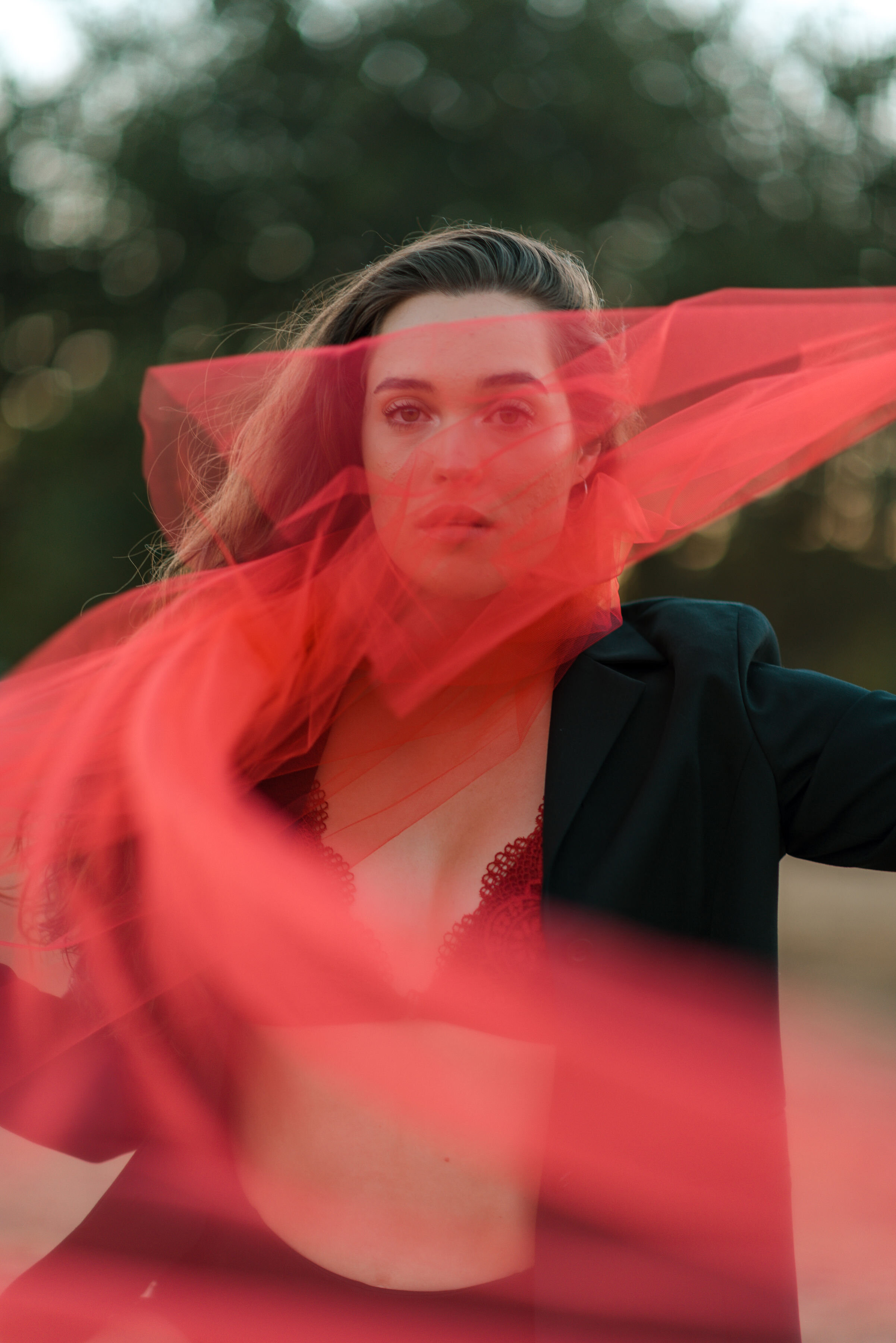 Lyndsi Seth Photography-A woman posing for a fashion portrait with a vibrant red fabric sheerly draped in front of her face and torso