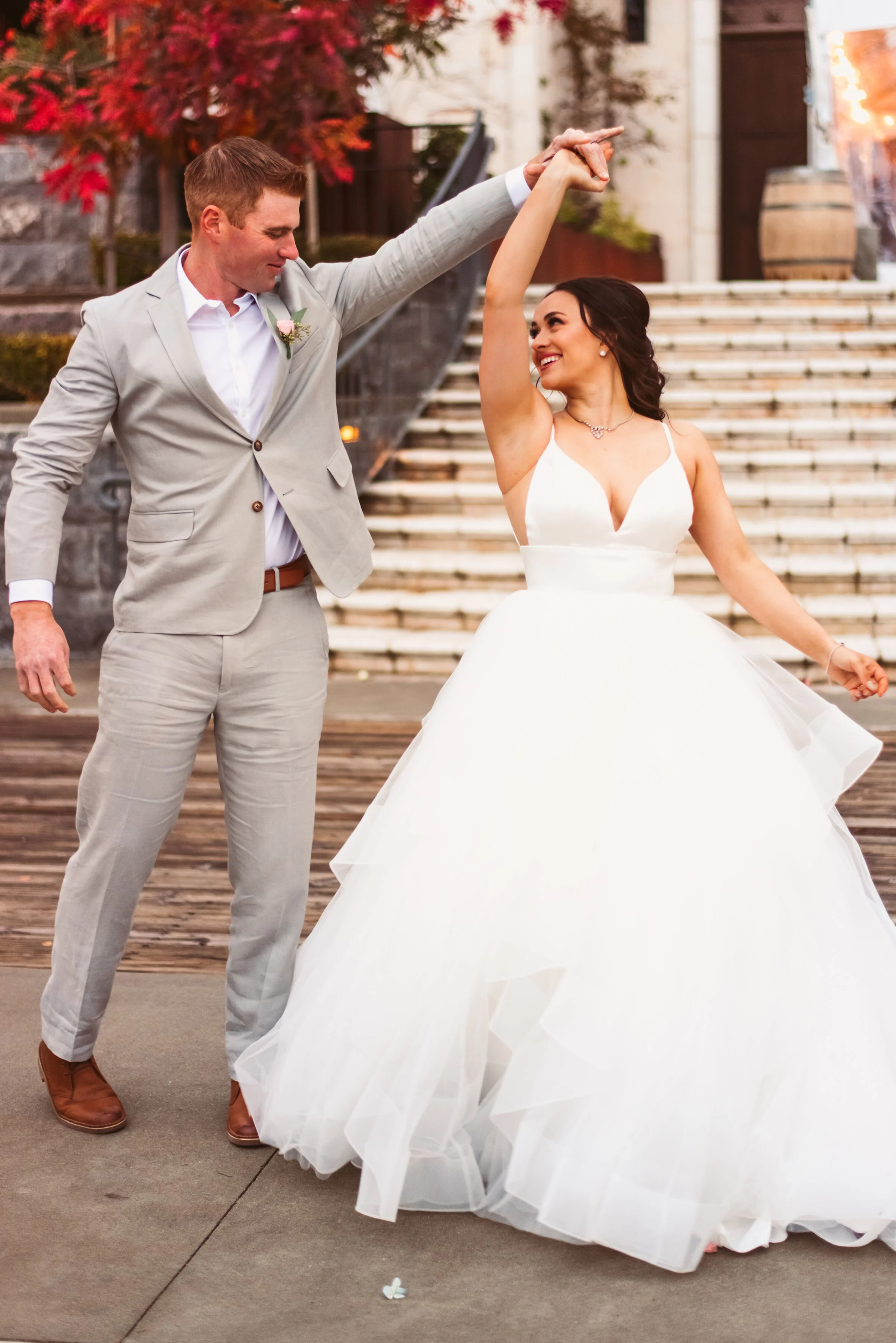 Lyndsi Seth Photography-A newlywed couple dancing outdoors, with the groom in a light grey suit twirling the bride in her white ballgown dress