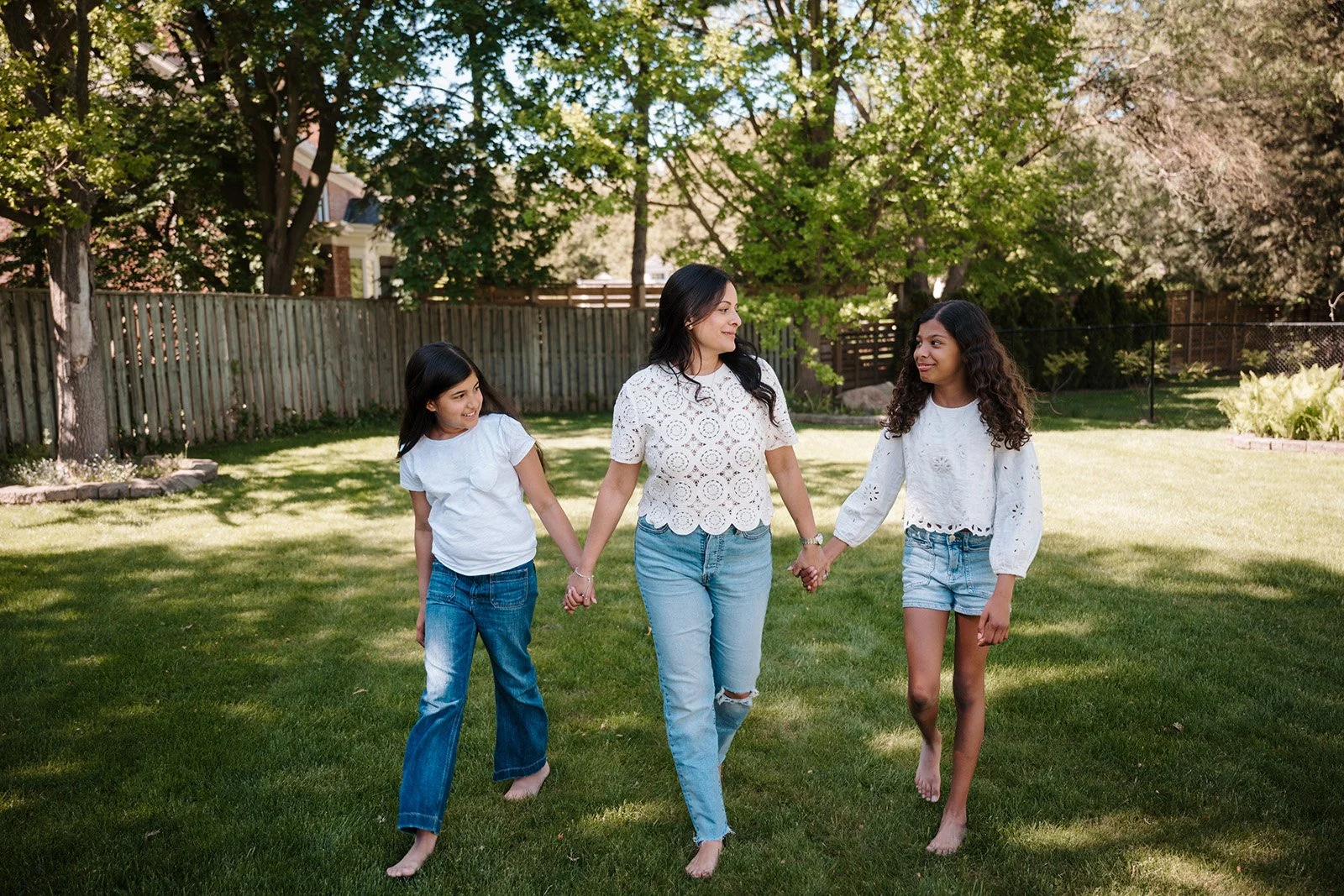 Lyndsi Seth photography- A mother and her two young daughters walking holding hands outside in a grassy yard