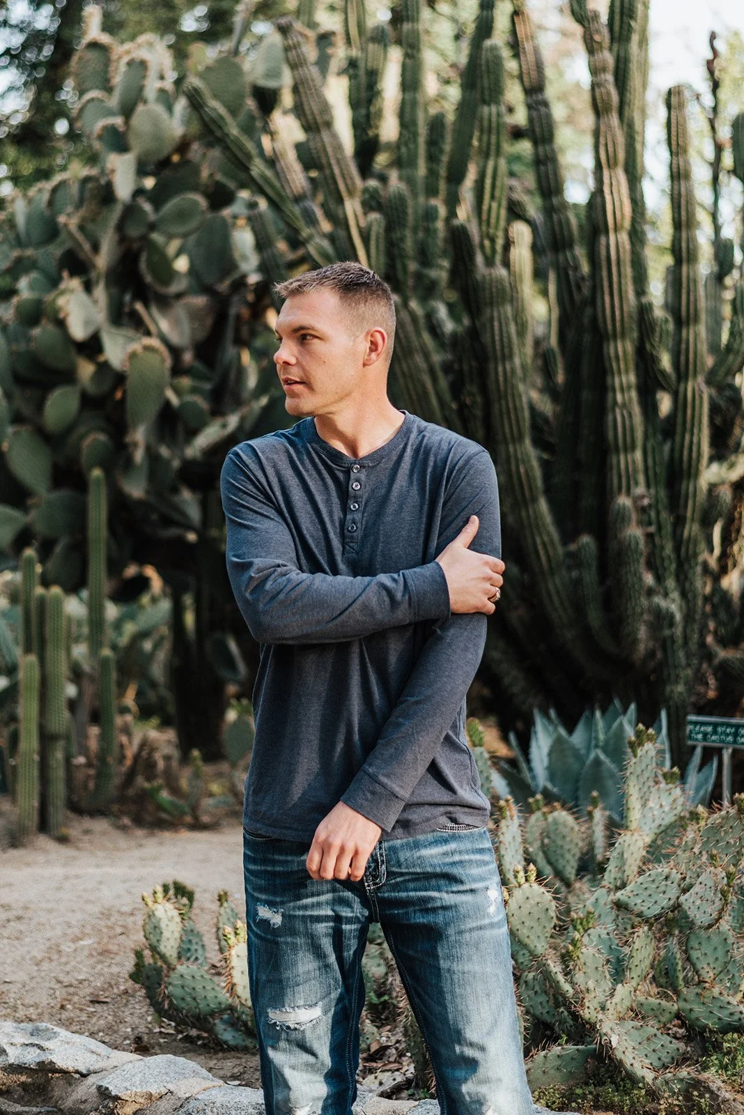 Lyndsi Seth photography- A man in a dark long-sleeve henley shirt crossing his arms while standing in front of large cacti