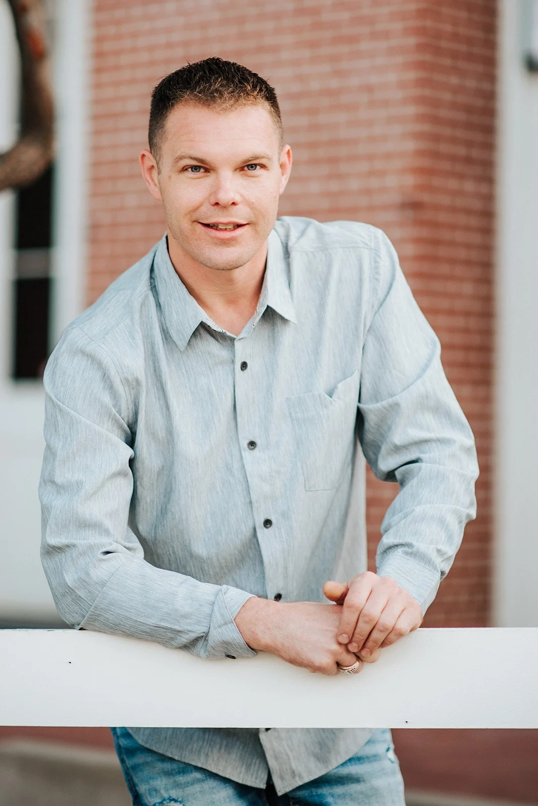 Lyndsi Seth Photography-A professional outdoor headshot of a man leaning on a railing and smiling