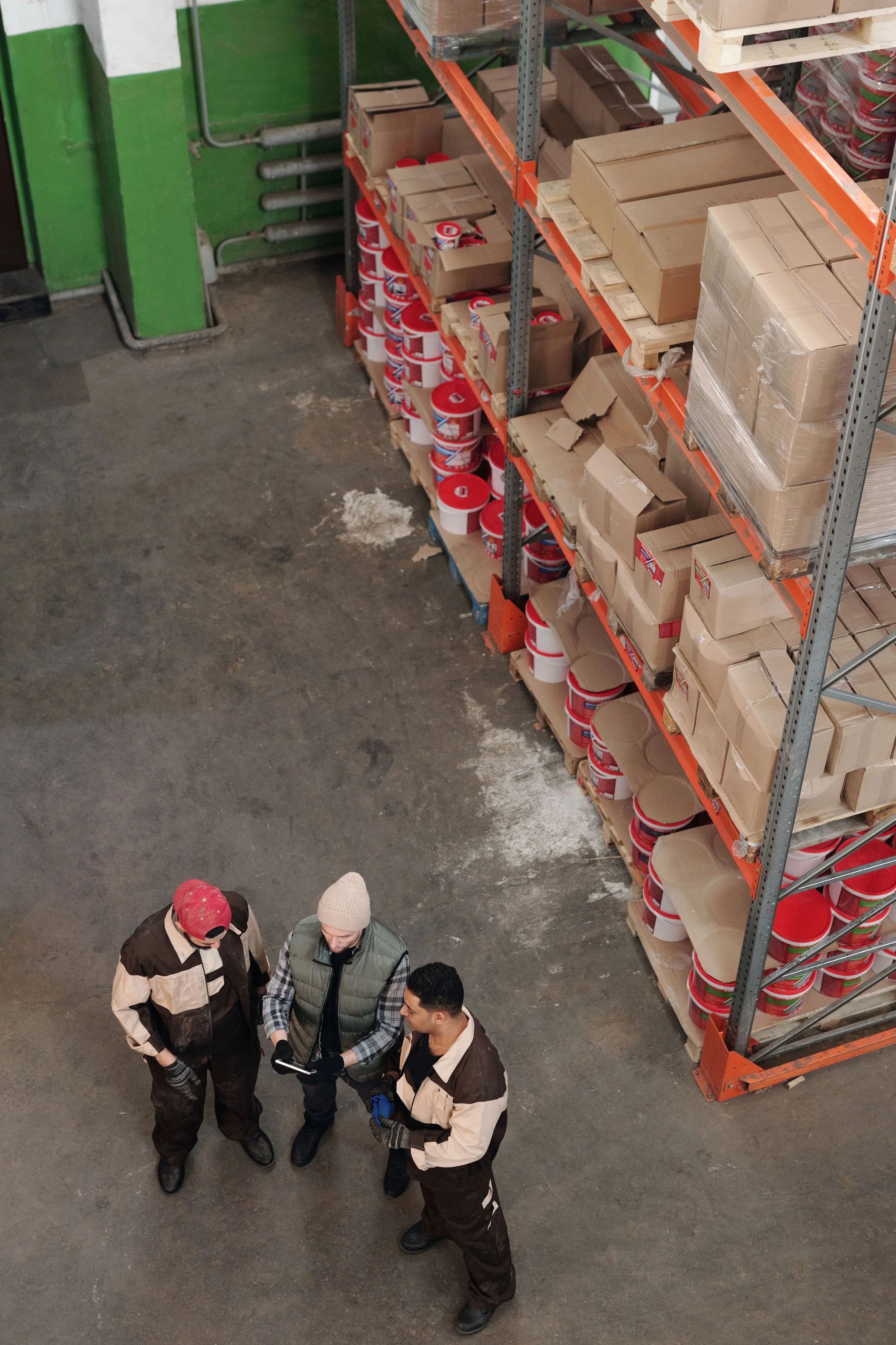 Three workers discussing inventory beside warehouse shelving.