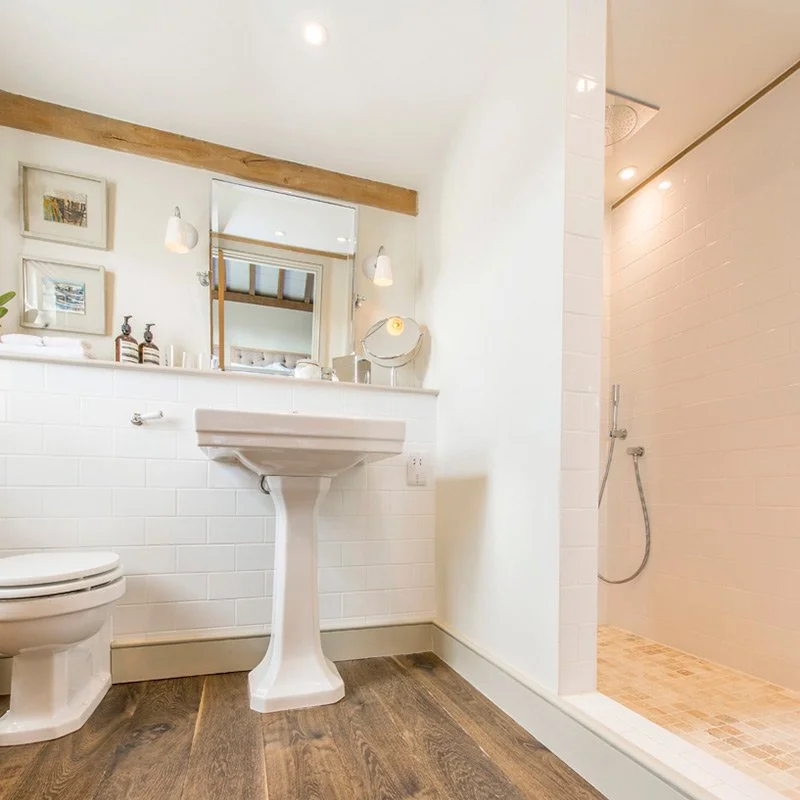 Bathroom with a toilet, a pedestal sink, a mirror, a shower area, and wooden flooring.