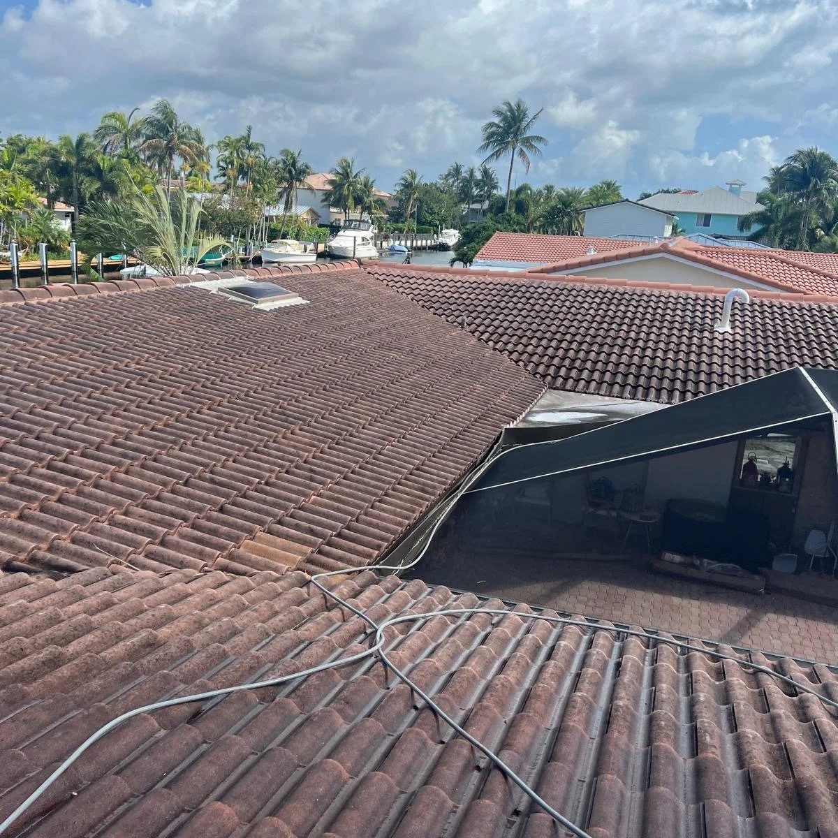 View of a neighborhood with red-tiled roofs, palm trees, boats, and a patio area under a partly cloudy sky.