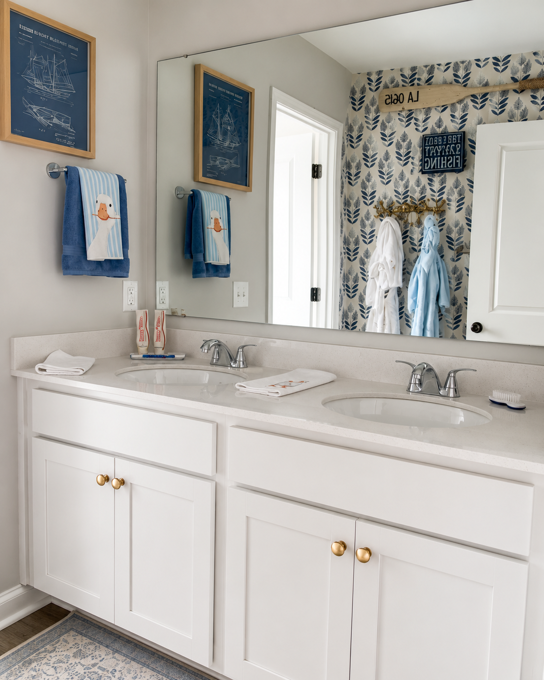 Bathroom with dual sinks, gold knobs, framed nautical blueprints, towel with duck embroidery, and nautical decor including oars and a wall-mounted coat rack with bathrobes.