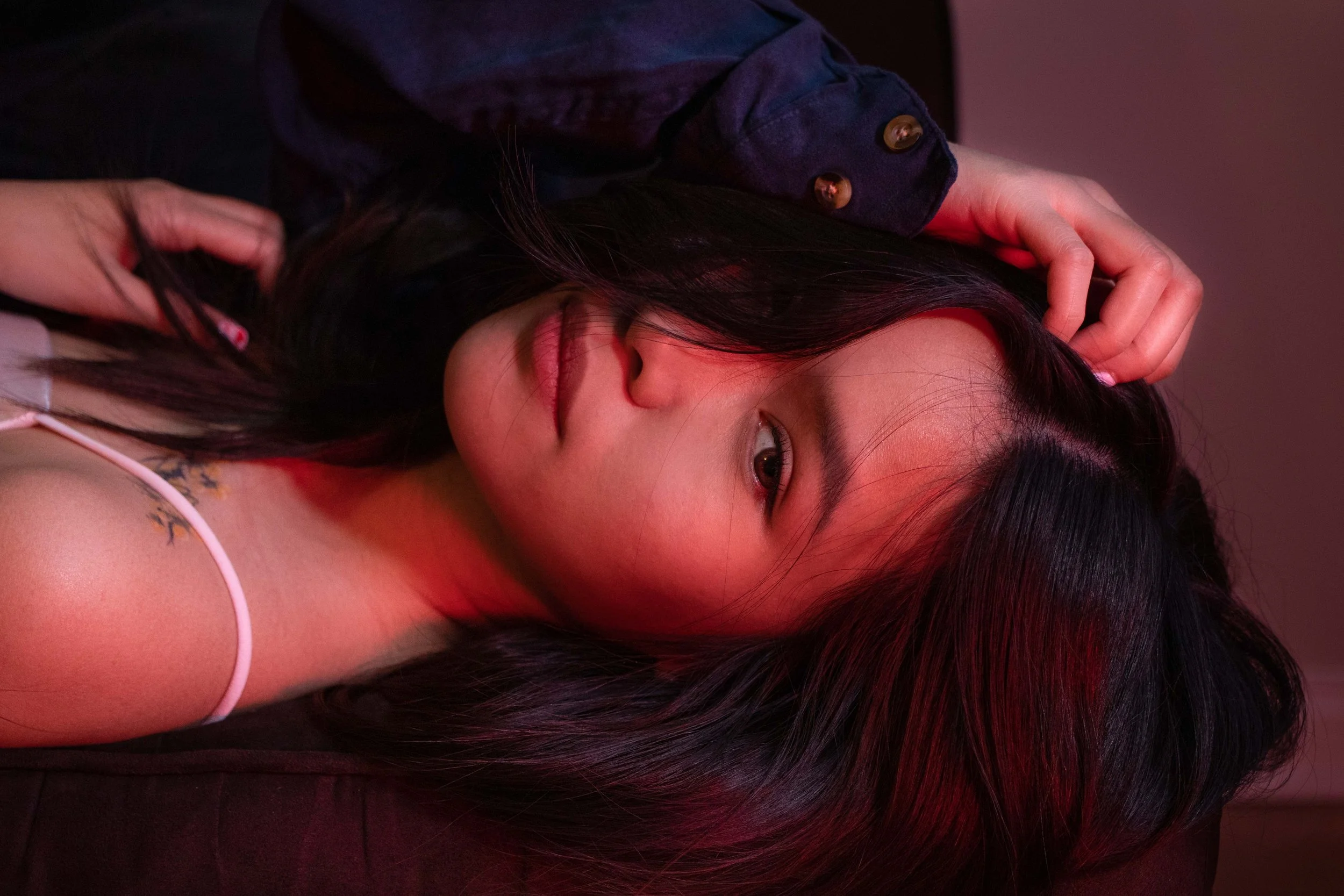 A woman with long dark hair lying down, resting her head on her hand, wearing a dark, possibly denim jacket.