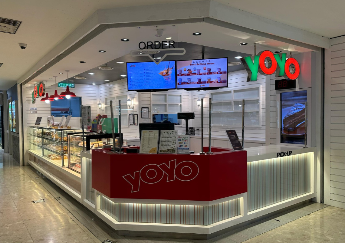 Yoyo bubble tea shop with red, green, and white signage, digital menu screens, and a display case with food items inside a shopping mall.