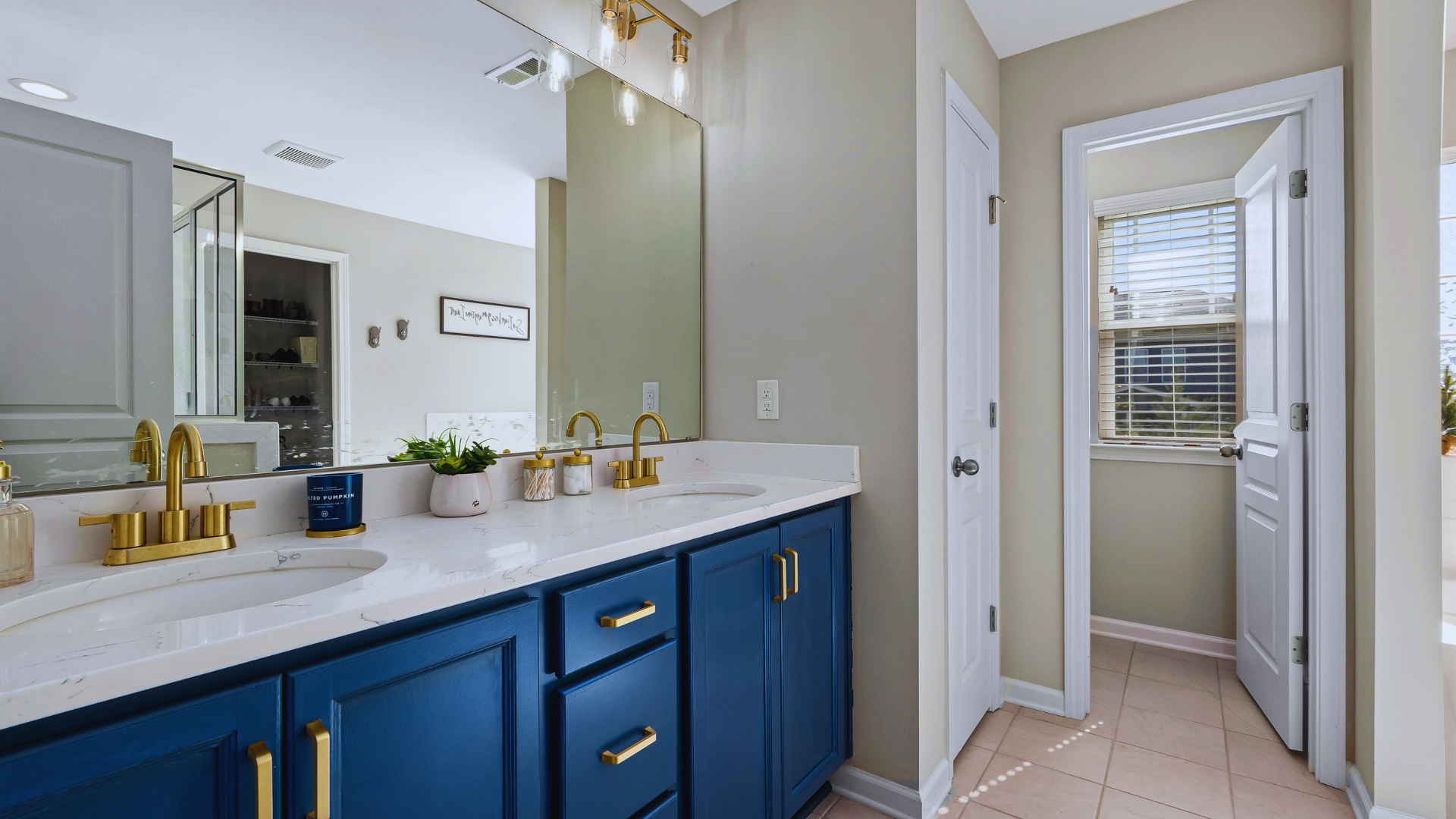 Bathroom with blue vanity, gold fixtures, large mirror, potted plant, and window with blinds