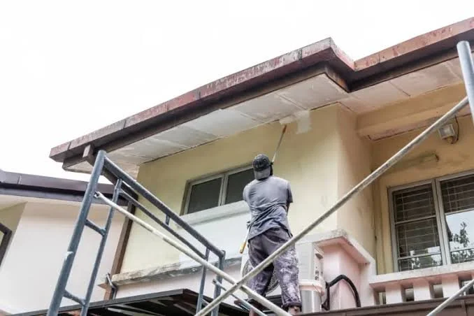 Worker on scaffolding painting the exterior wall of a house