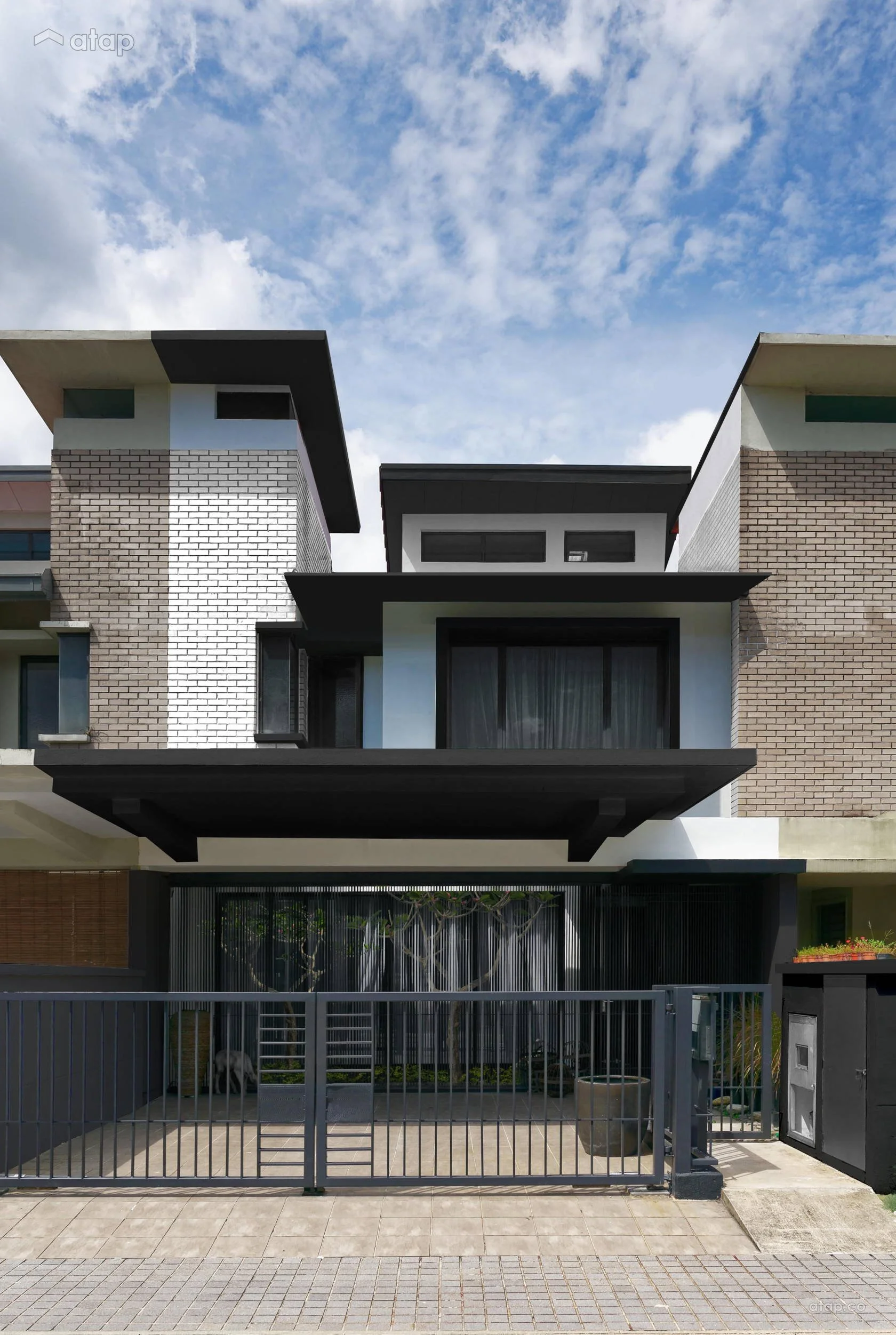 Modern multi-story house with brick and white exterior, black accents, large windows, and a gated front entrance with a dog inside.
