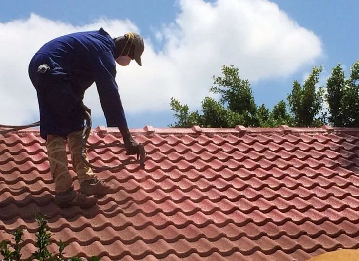 Person in dark clothing and a hat inspecting a red tiled roof from a ladder or height