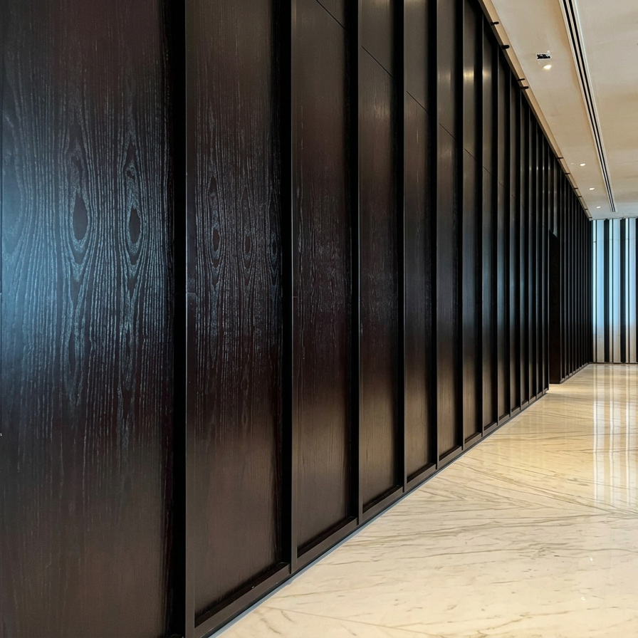 Interior view of a modern building hallway with dark wood paneling on the wall and a light-colored marble floor.