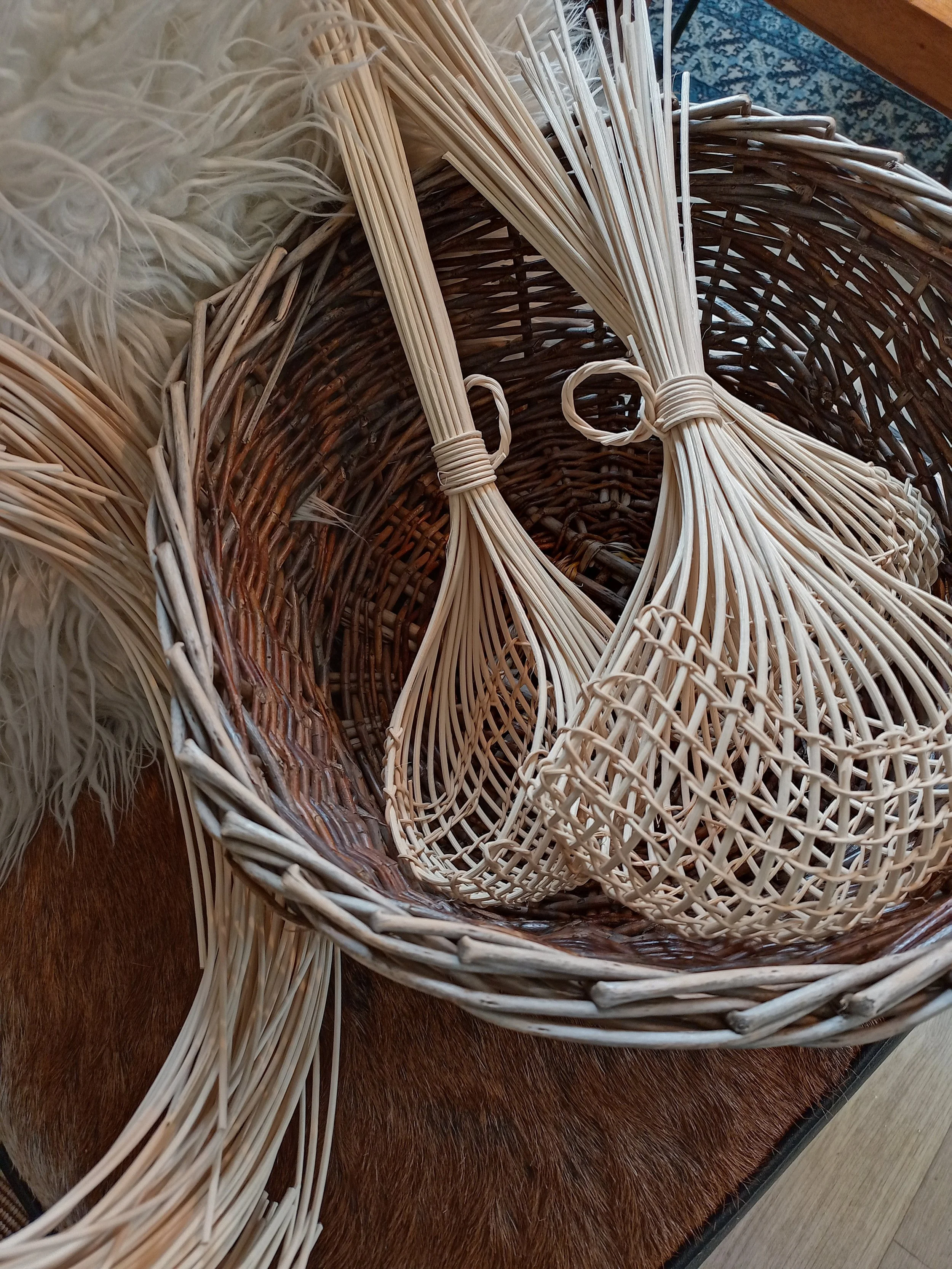 A woven wicker basket with some long, thin wooden sticks tied with small rubber bands resting inside it, placed on a wooden surface.