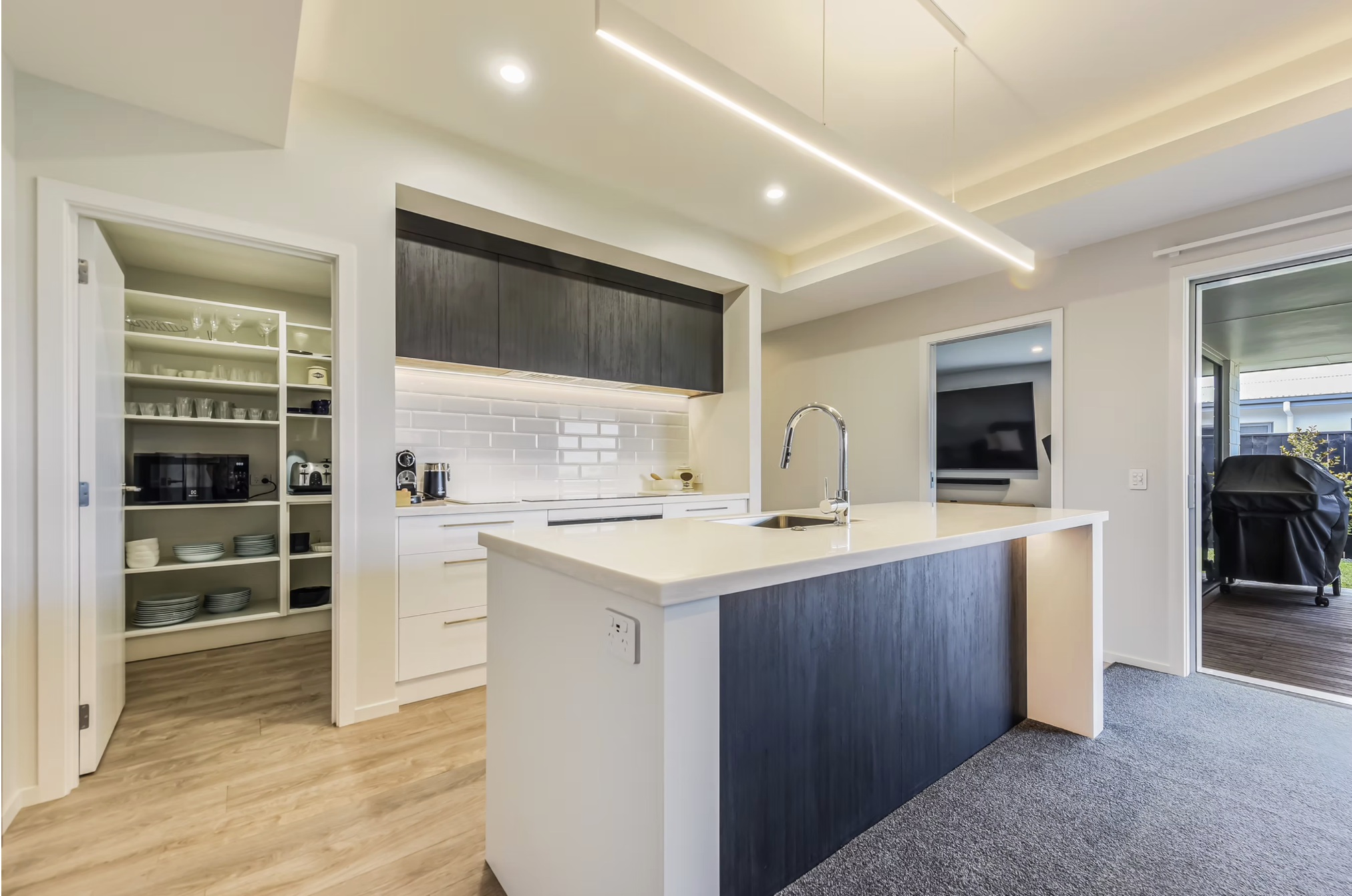 Open-concept kitchen with white and dark wood cabinetry, a white island with a sink, and built-in appliances. Sliding glass door leads to an outdoor area with a chair.