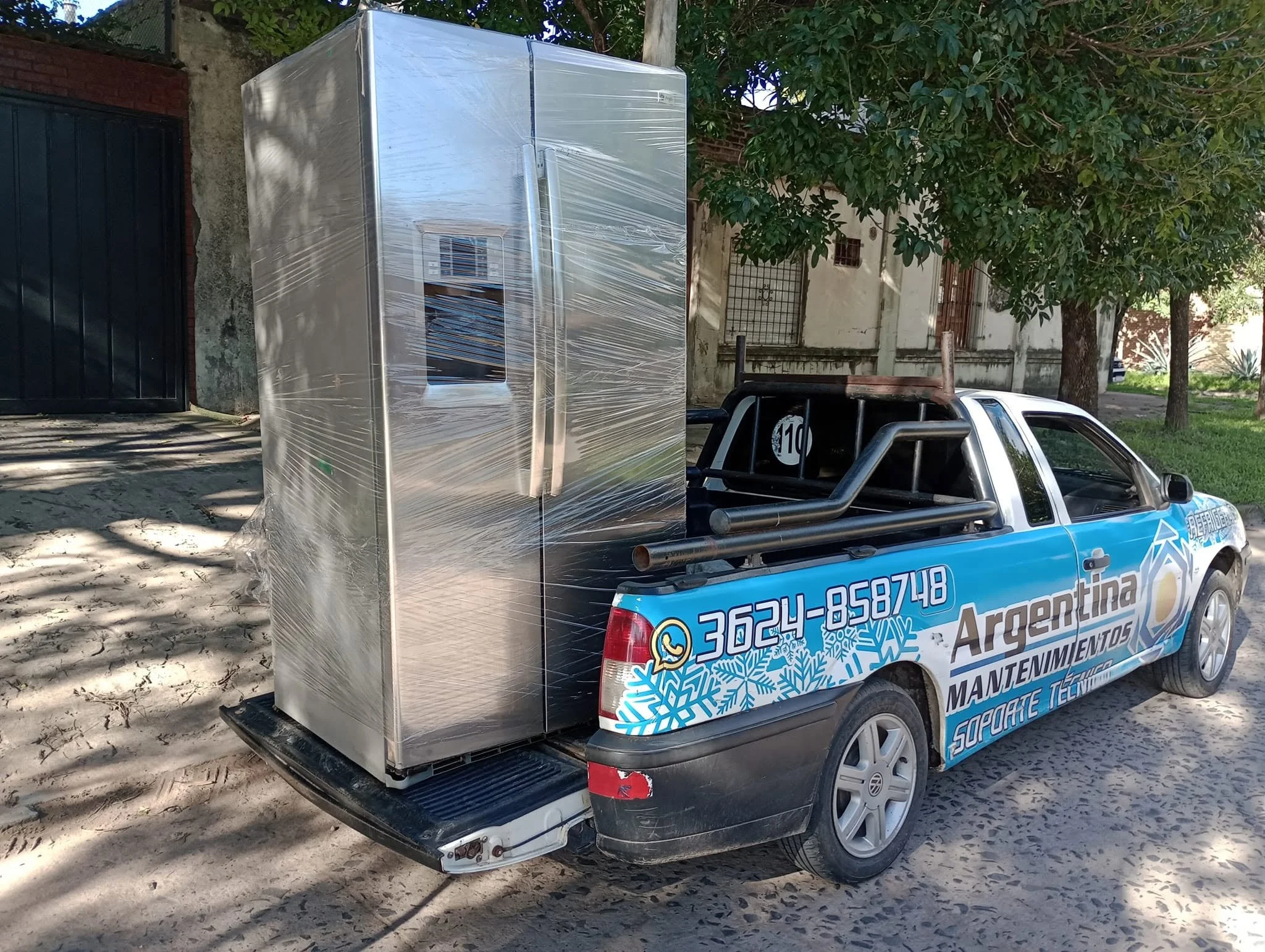 Camioneta de seguridad municipal con cartel que tiene info de mantenimiento y servicios, con una máquina de aire acondicionado o refrigeración instalada en la parte trasera, en un área de árboles y casas.