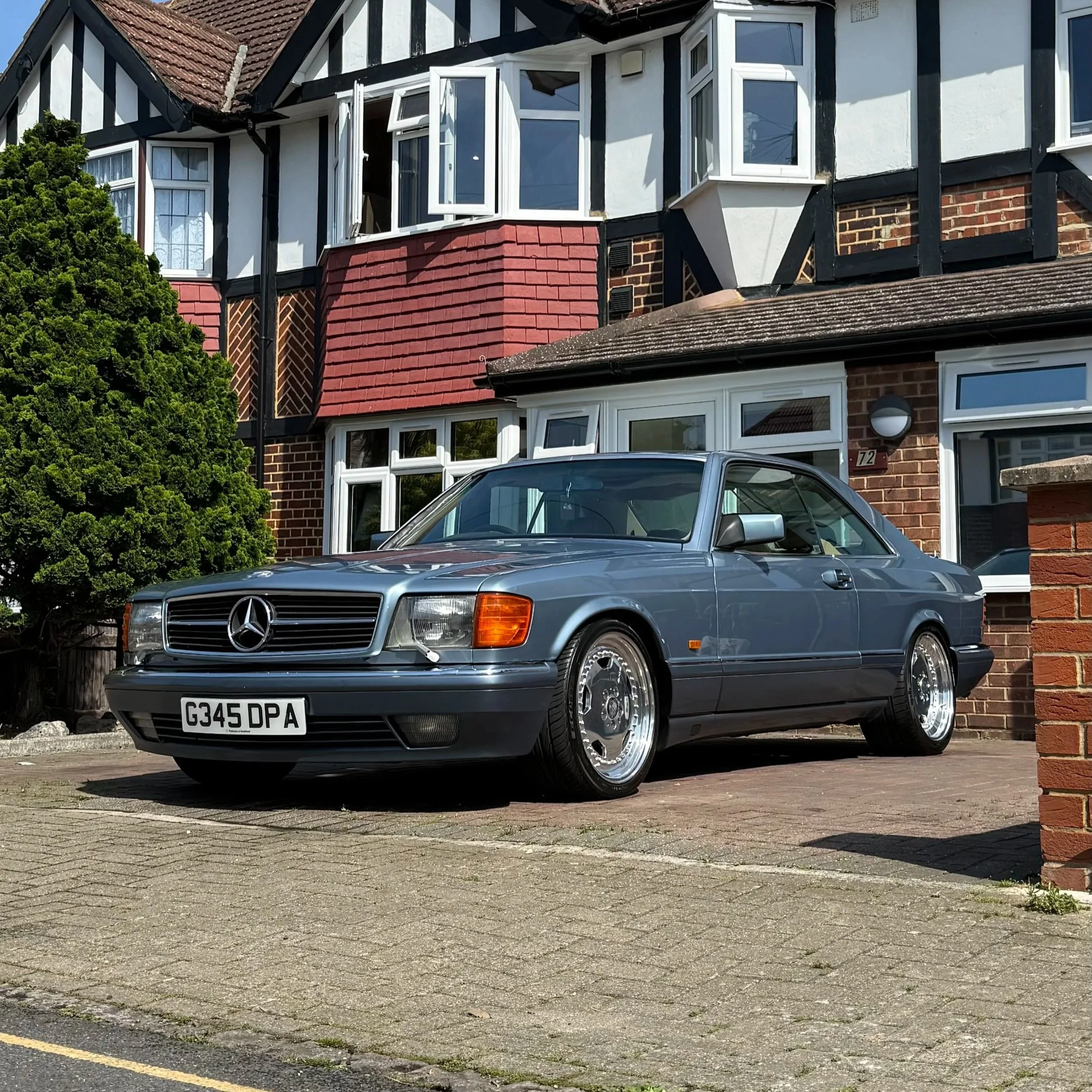 A silver Mercedes-Benz car parked on a residential driveway in front of a brick and black-and-white timber-framed house with white windows and a red tiled roof.