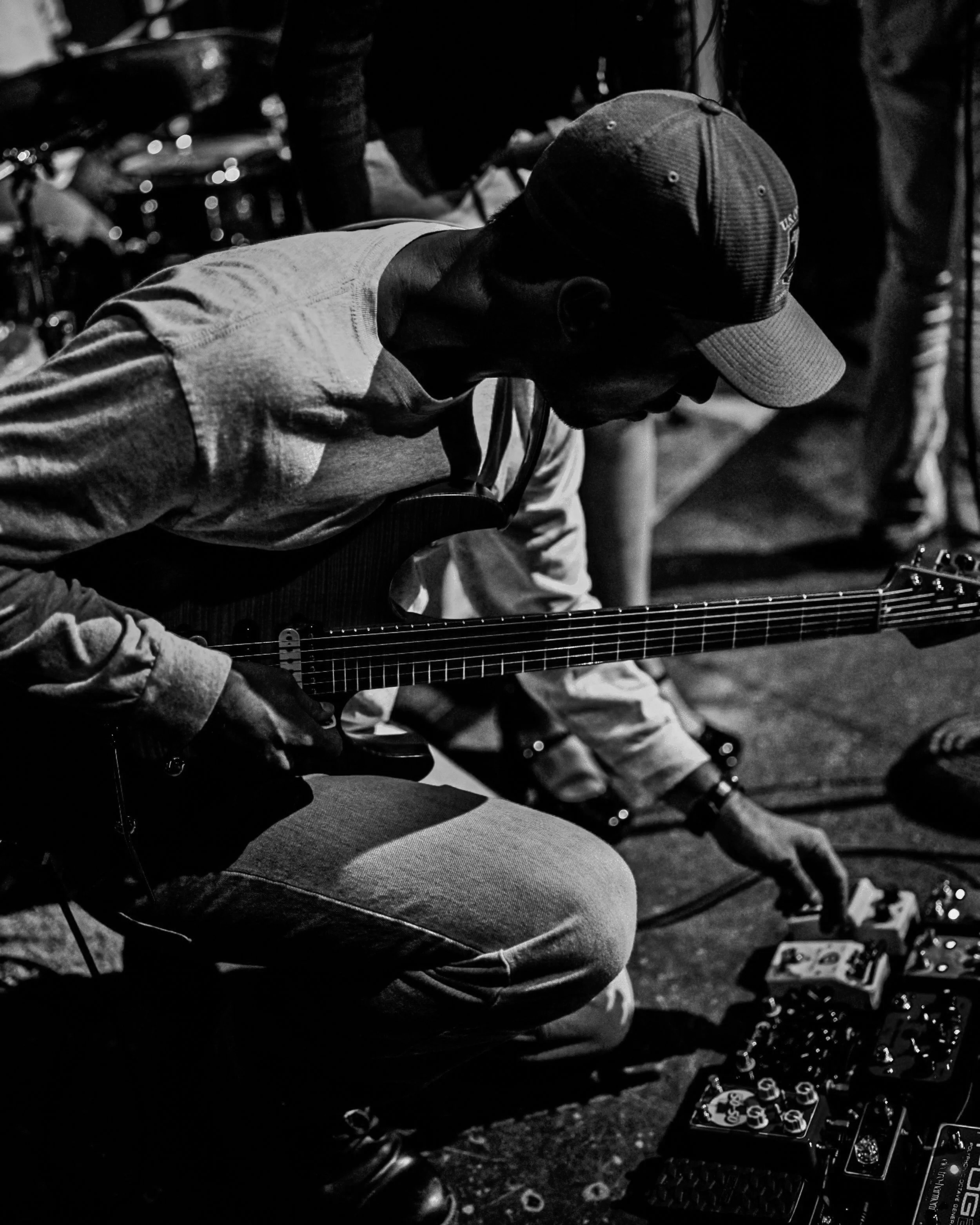 A man wearing a baseball cap and casual clothing is playing a guitar, sitting outdoors at night. The scene is dimly lit, with some musical equipment visible.  Nashville Guitar Lessons Zoom Guitar Lessons Virtual Lessons In Person Guitar Lessons