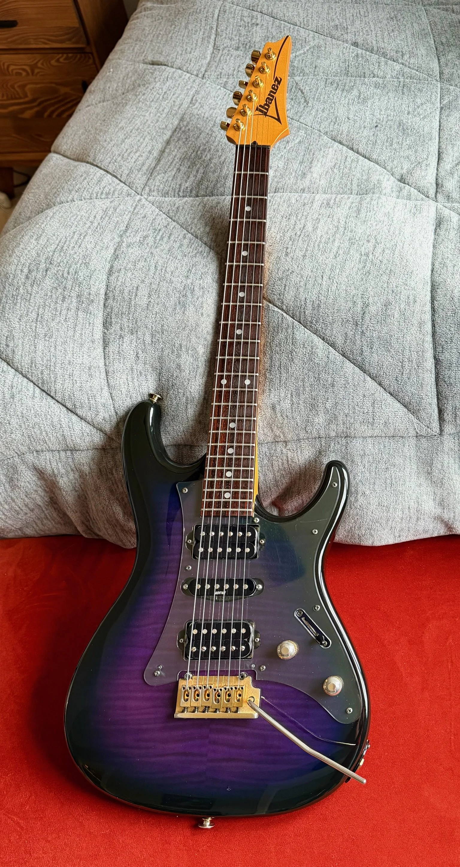 Electric guitar with a purple burst finish, lying on a red and gray fabric surface.