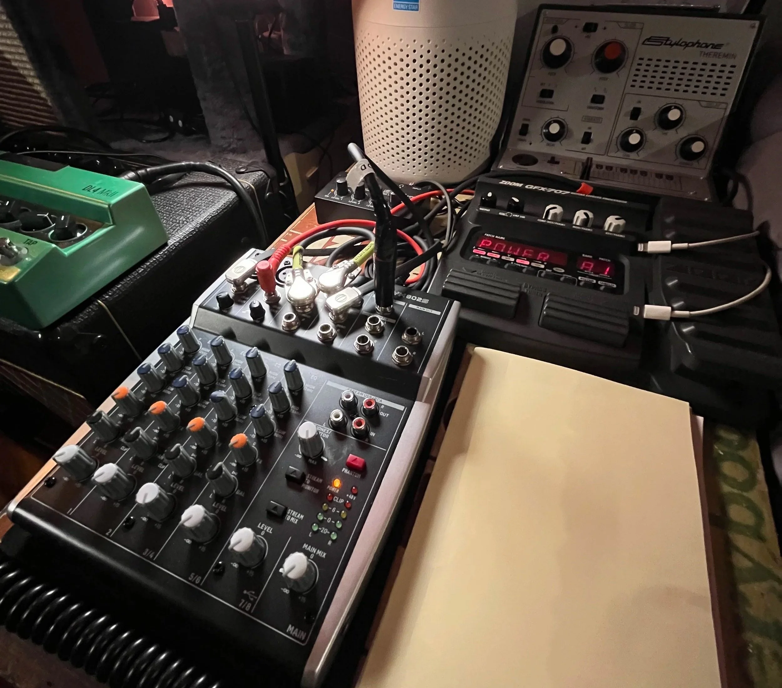 A collection of electronic music equipment including a mixer, a multi-effects pedal, various cables, and other synthesizer and audio devices on a table.