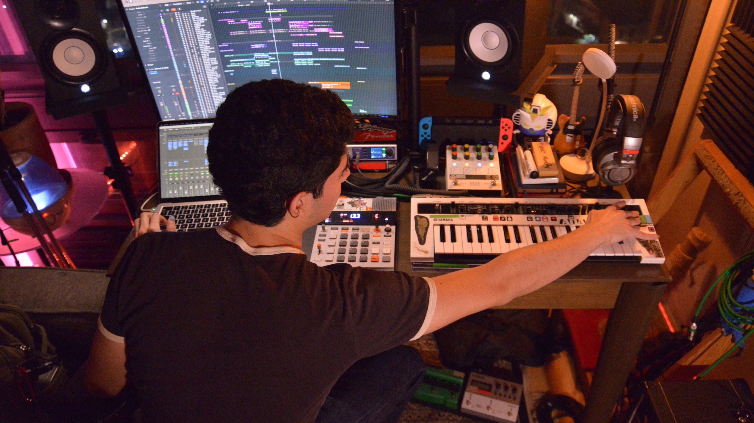 A person working in a music studio with multiple electronic musical instruments, monitors, and headphones.