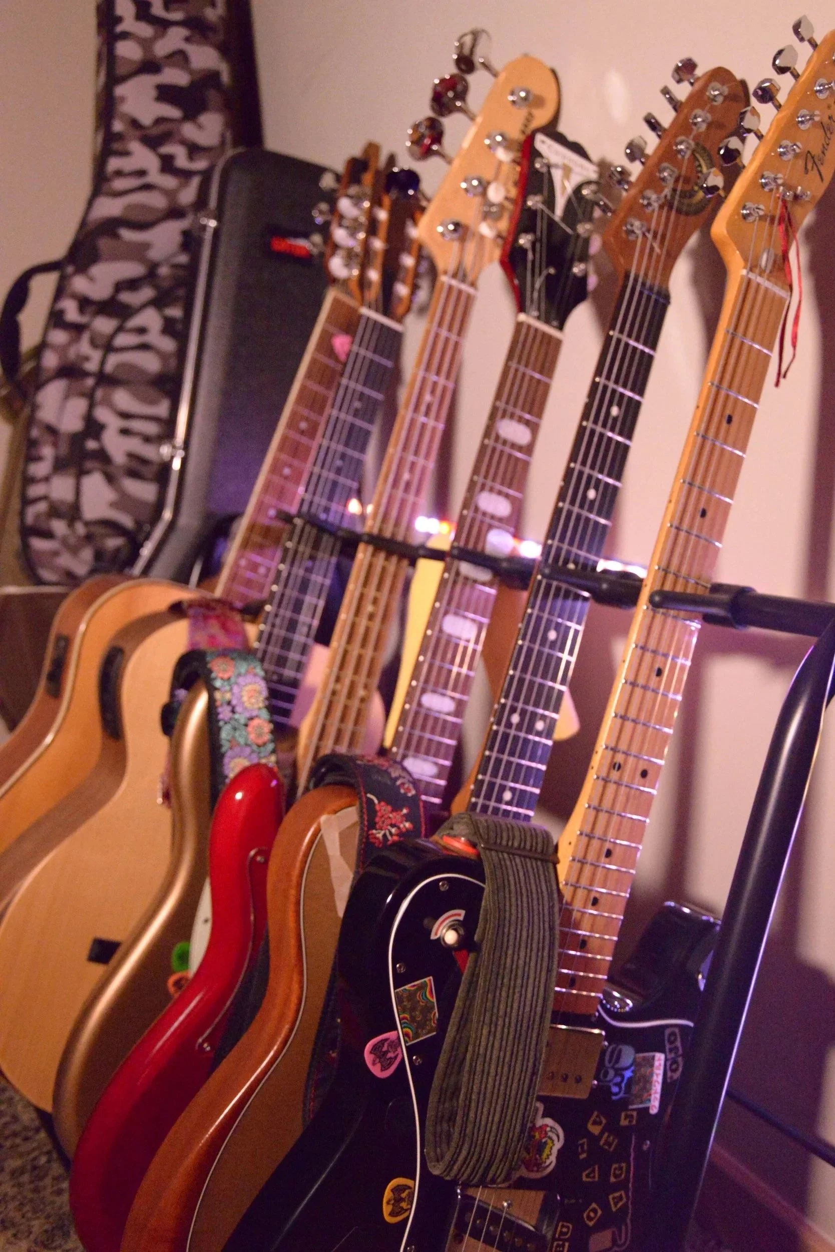 A collection of various guitars hanging on a wall in a room, with different styles and colors, including acoustic and electric guitars.