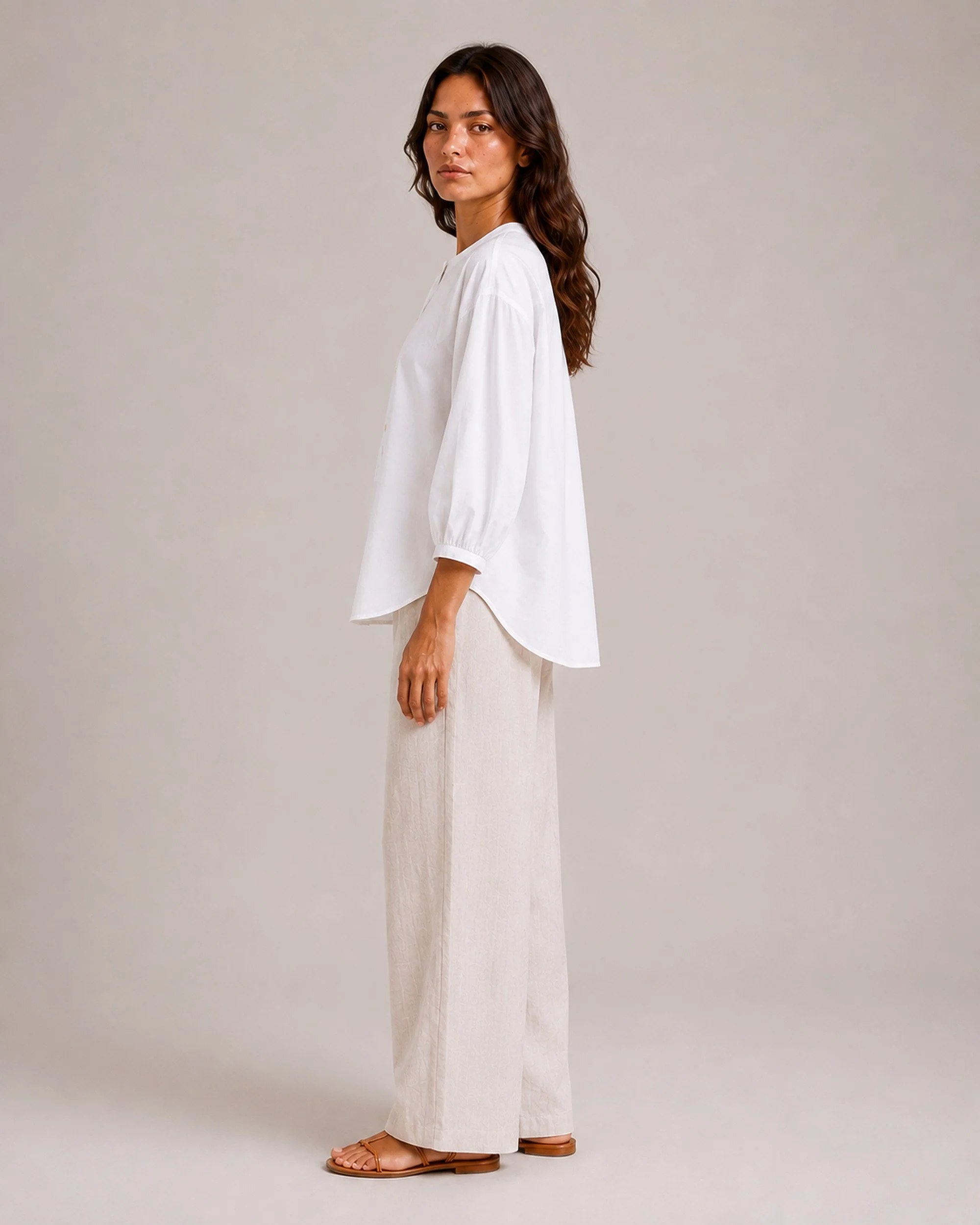 Side view of The Flax Studio white Voluminous Cotton Top, showing its curved hem and gathered sleeve cuff.