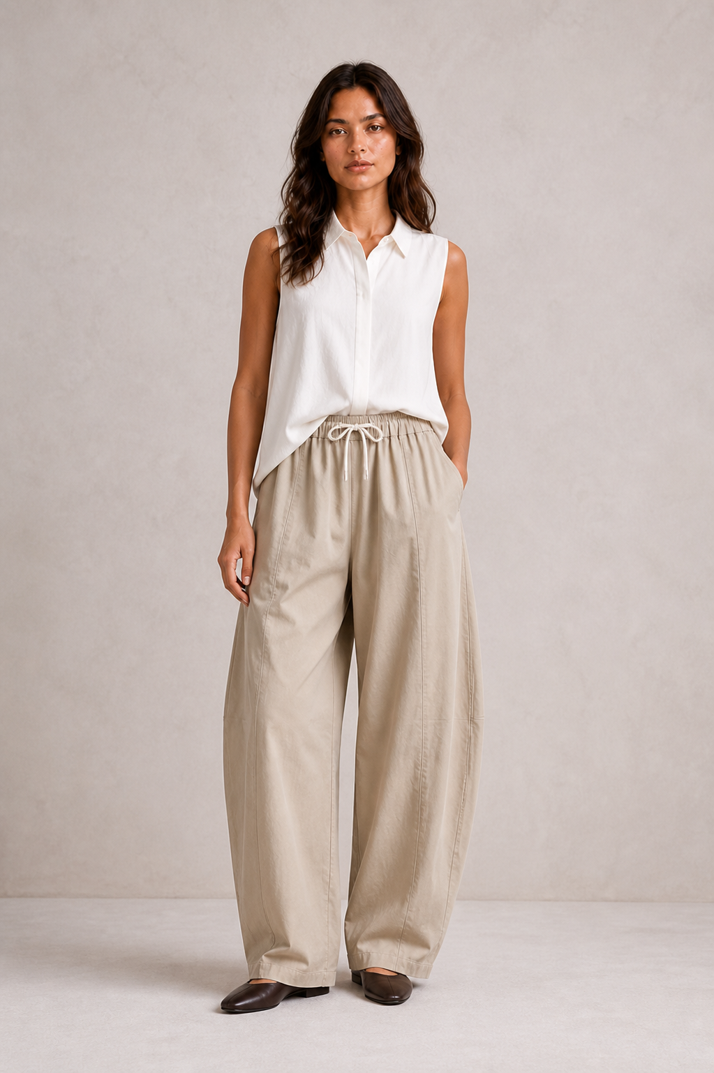 The Flax Studio Esme Pant in tan, styled with a white sleeveless top, showing the relaxed curved-leg silhouette.