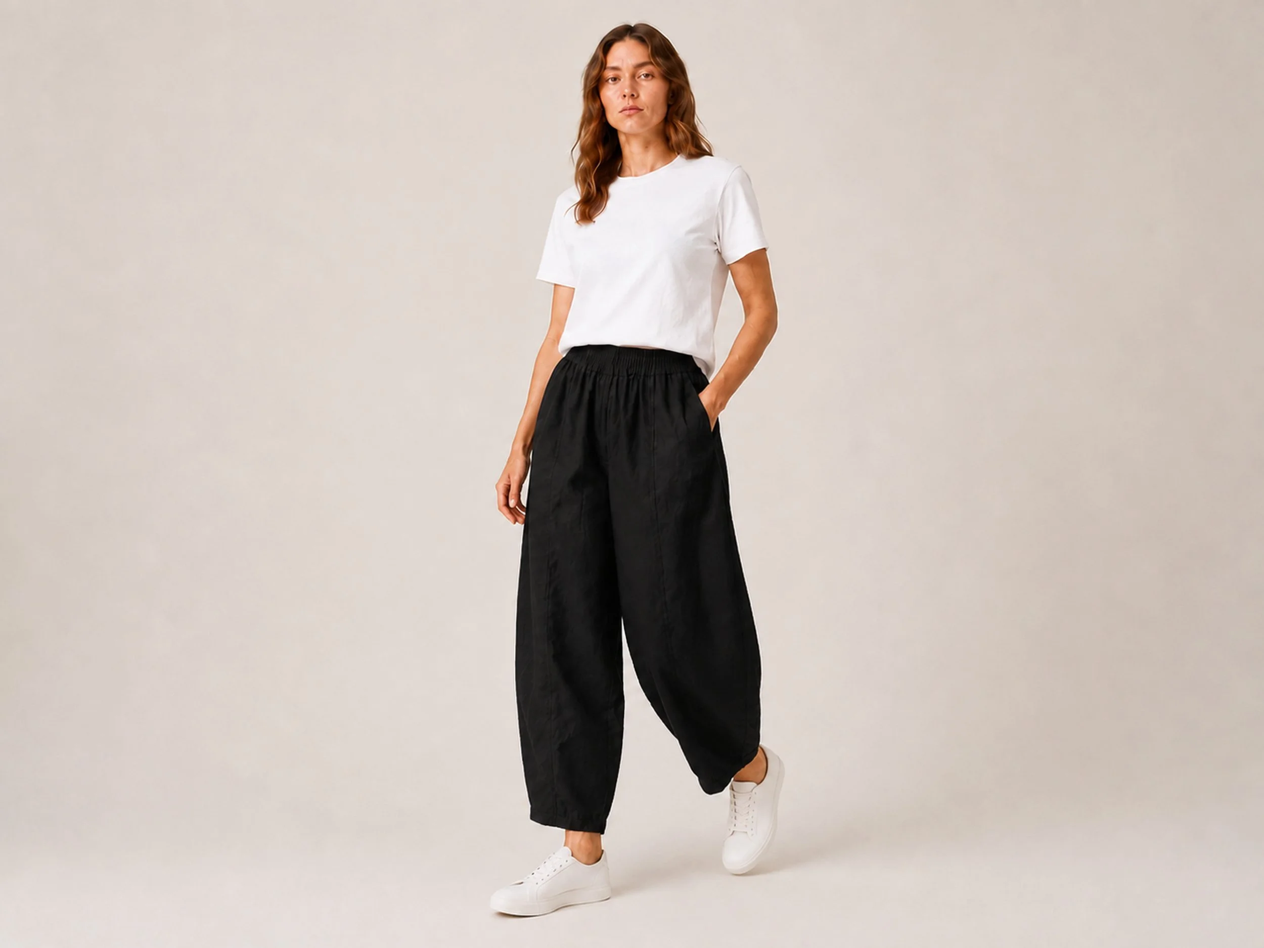 The Flax Studio black Sculpted Cotton Pant worn in motion with a white T-shirt and white shoes.